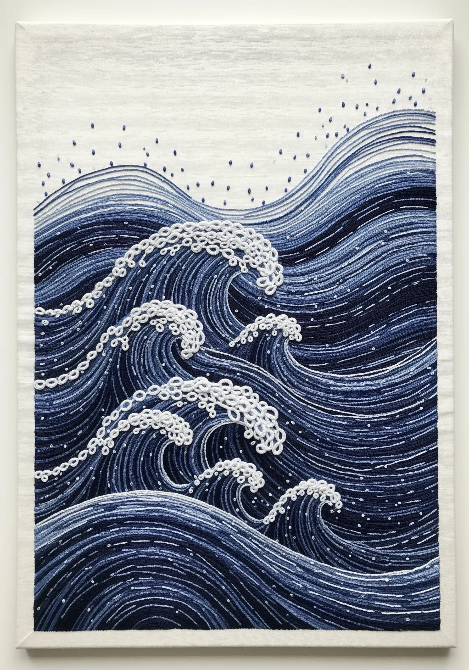 Embroidery of deep blue ocean waves with white French knot foam, showcasing directional stitching.