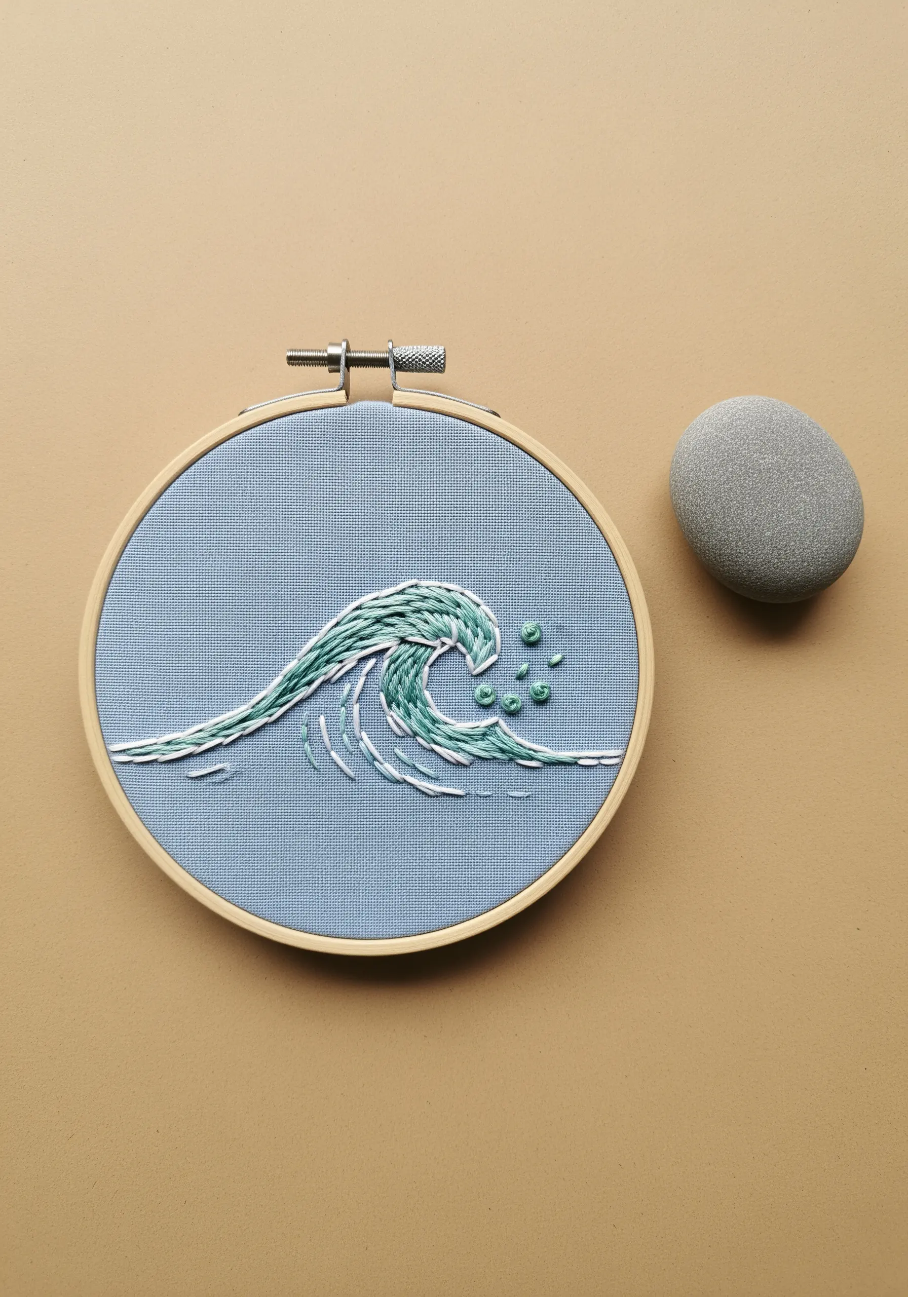 An embroidered ocean wave using layered straight stitches in shades of green and white.