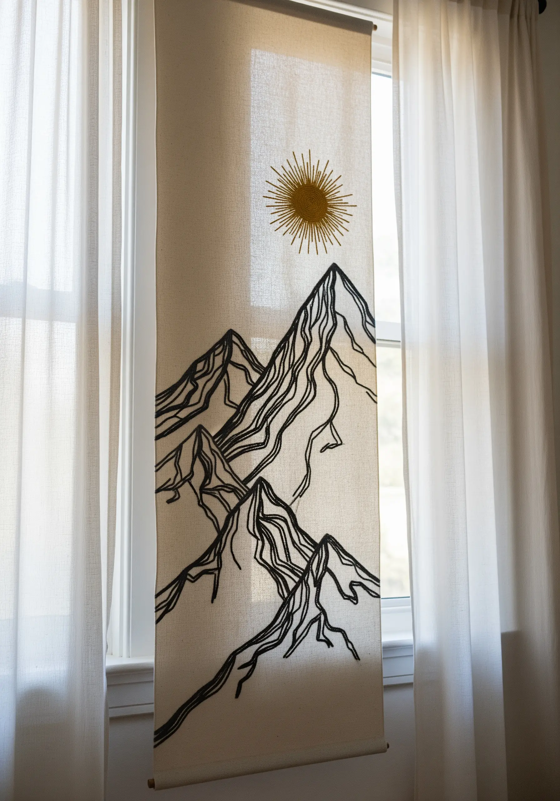 Minimalist line art embroidery of mountain peaks on a linen wall hanging.