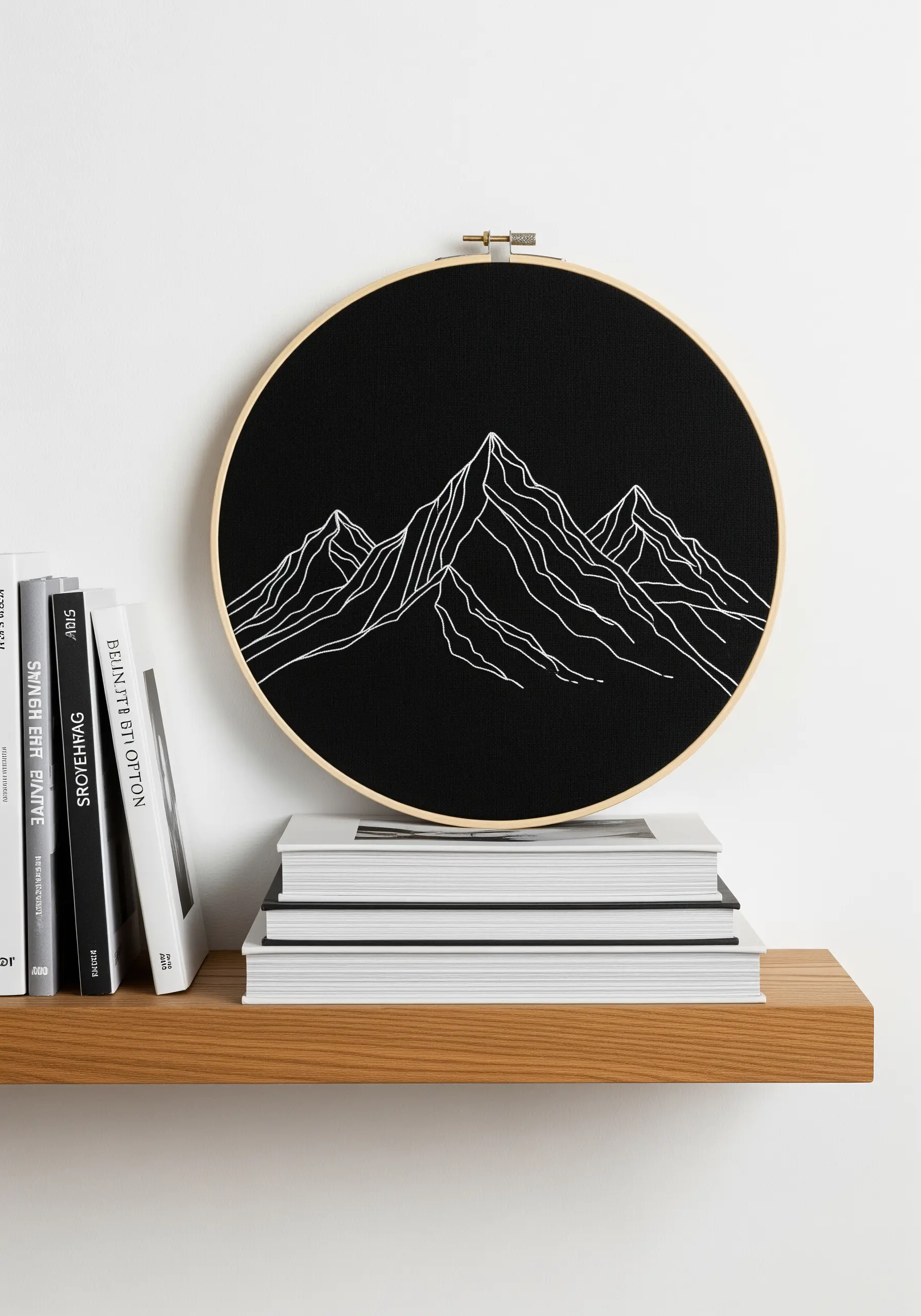 White-thread line art embroidery of mountain peaks on black fabric in a hoop.