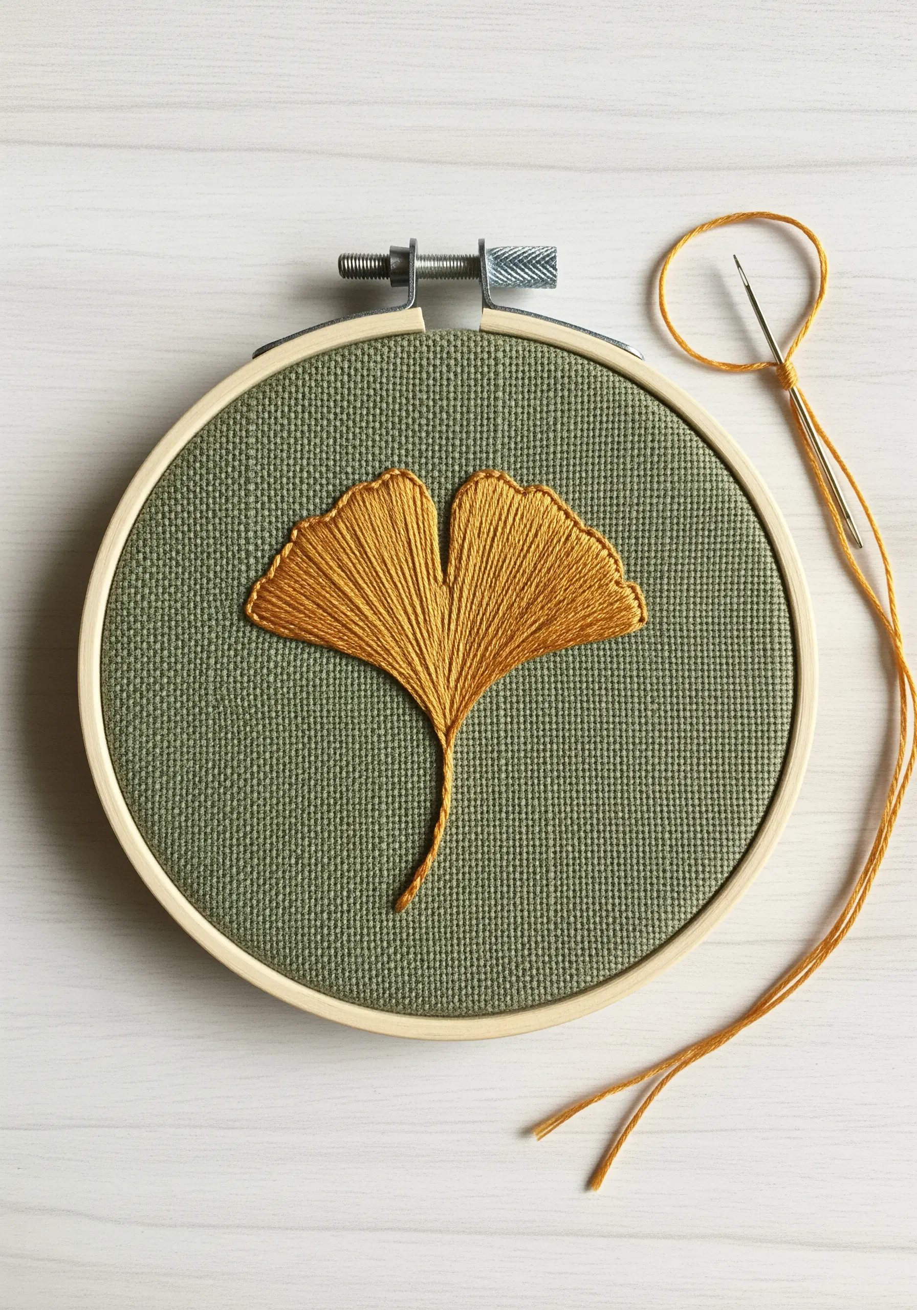 A golden-yellow ginkgo leaf embroidered on olive green fabric, showing fanned satin stitches.