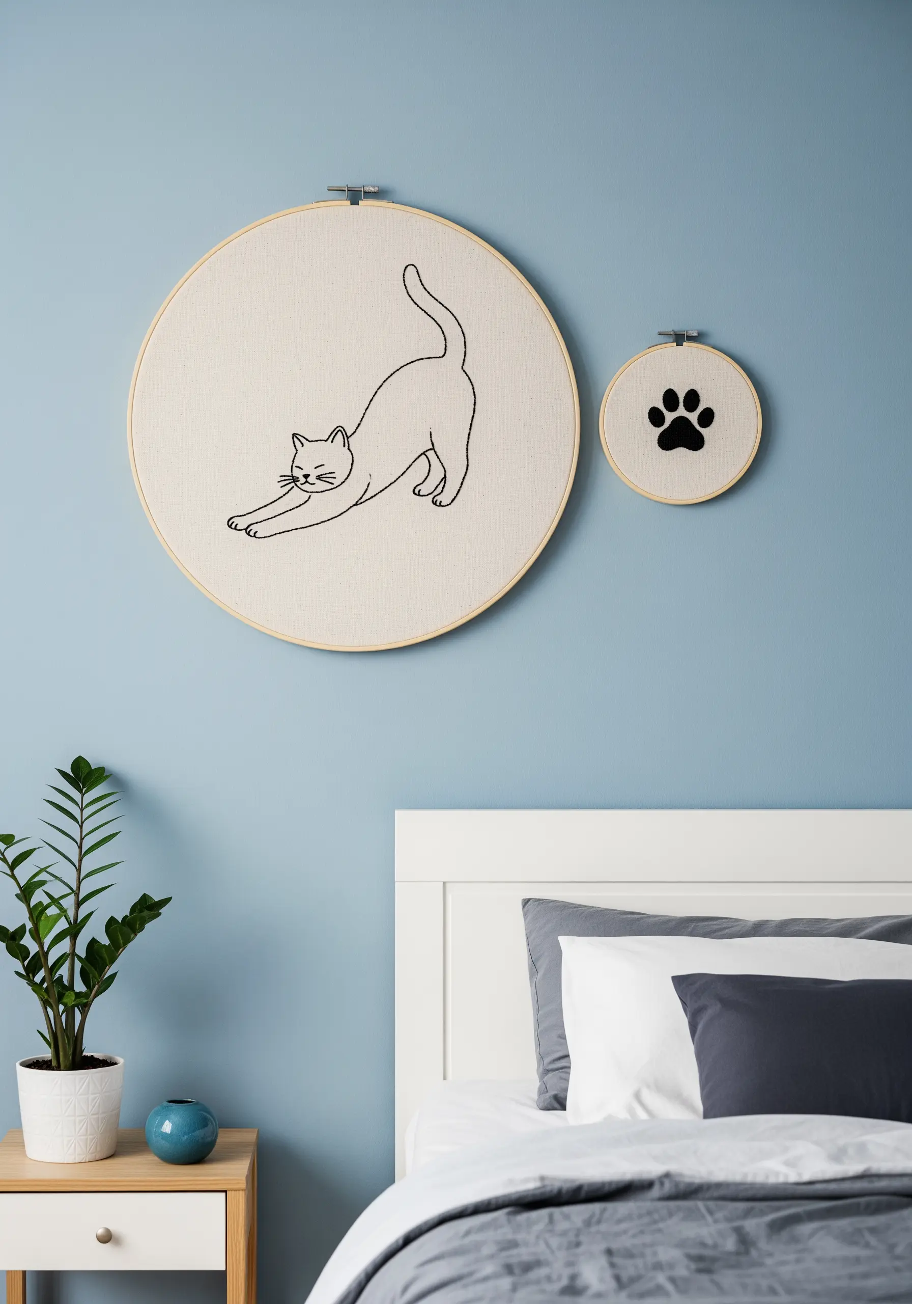 A minimalist line art embroidery of a stretching cat paired with a small paw print hoop.