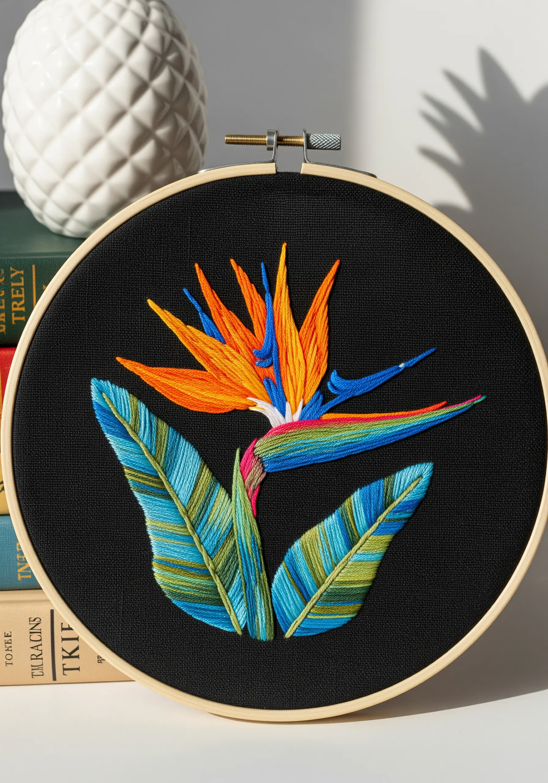 Vibrant thread-painted bird of paradise flower on black fabric in an embroidery hoop.