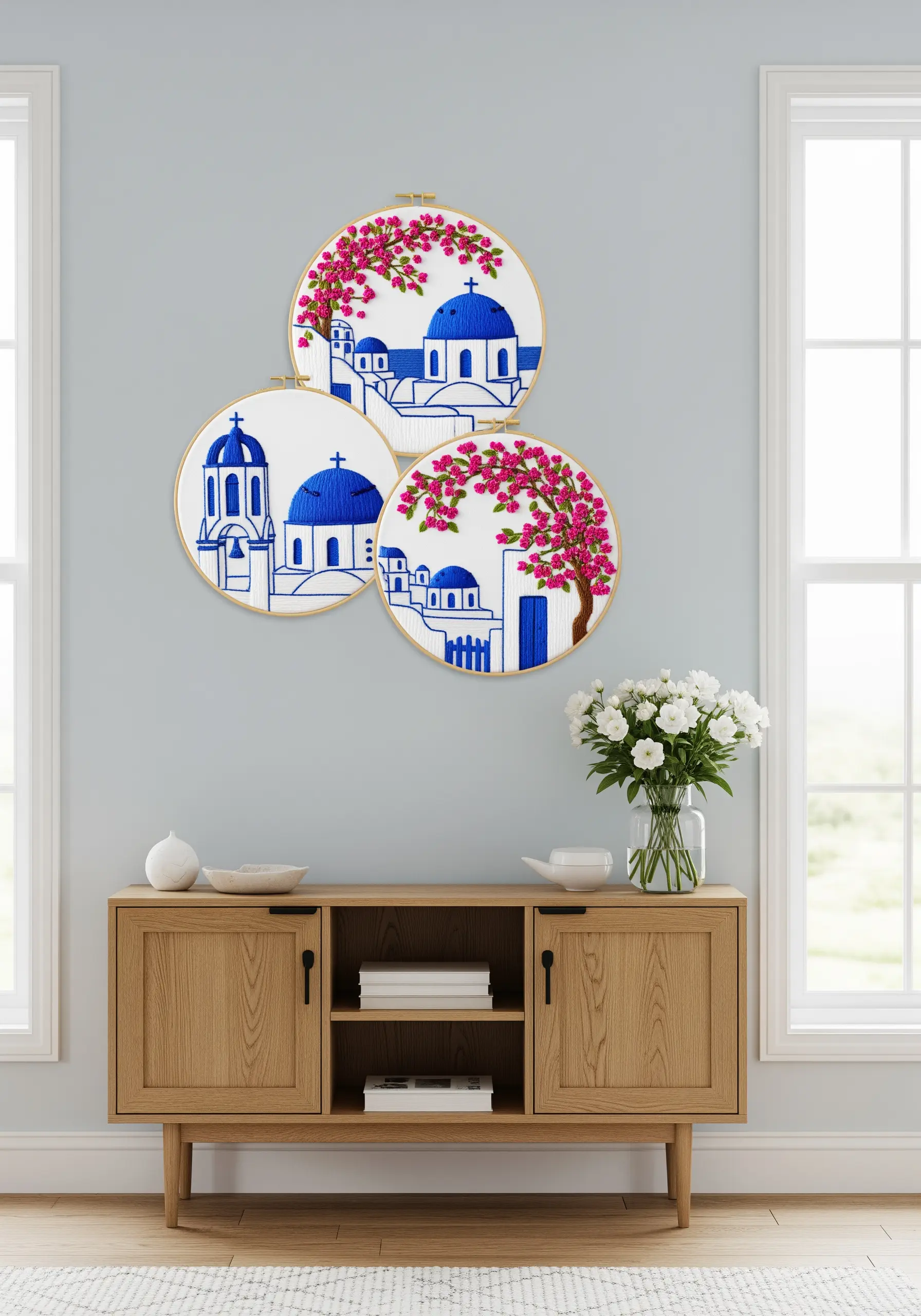 Triptych of embroidery hoops showing Santorini's blue-domed buildings and pink bougainvillea.