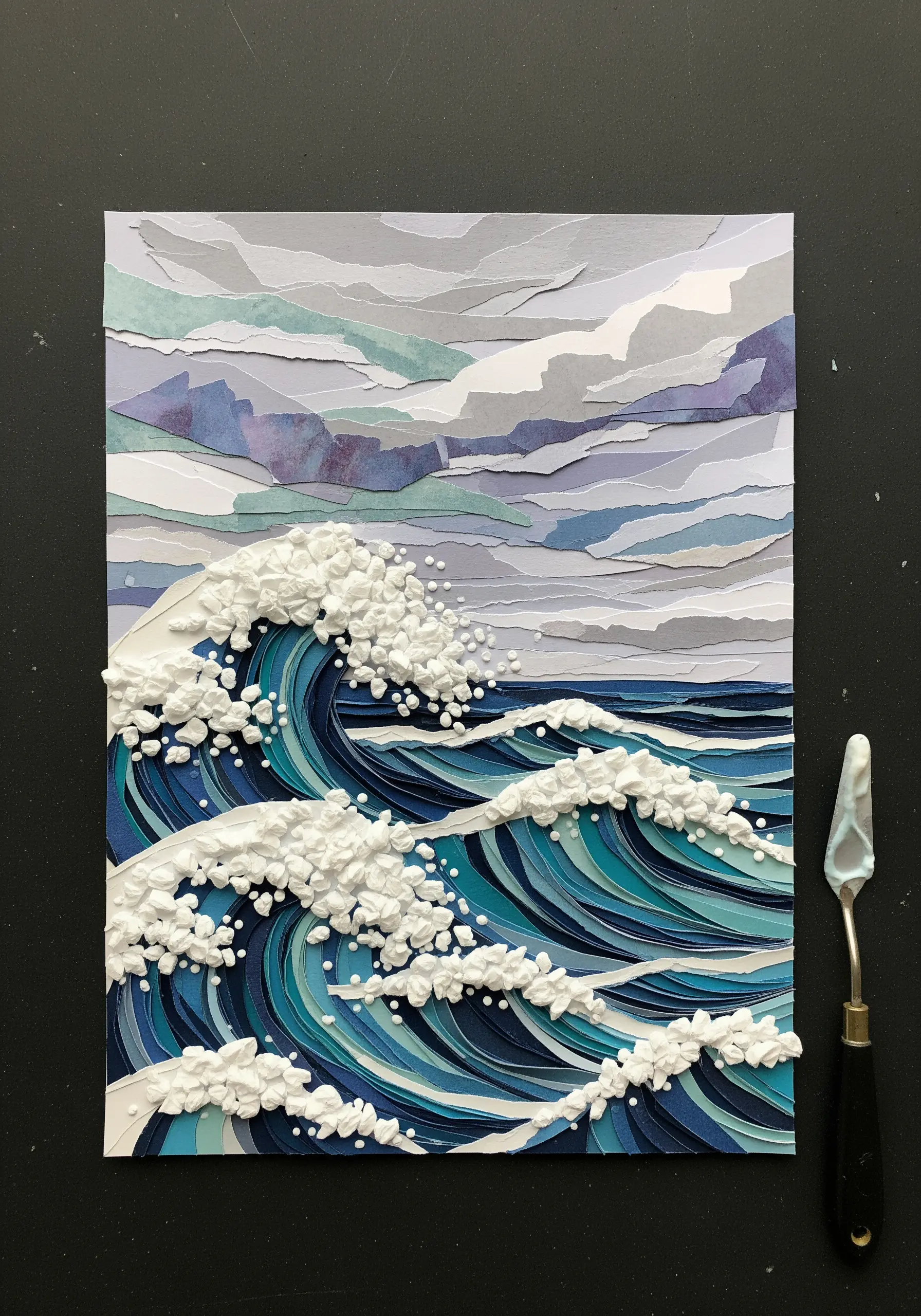 A paper collage of ocean waves with dimensional, textured white sea foam.