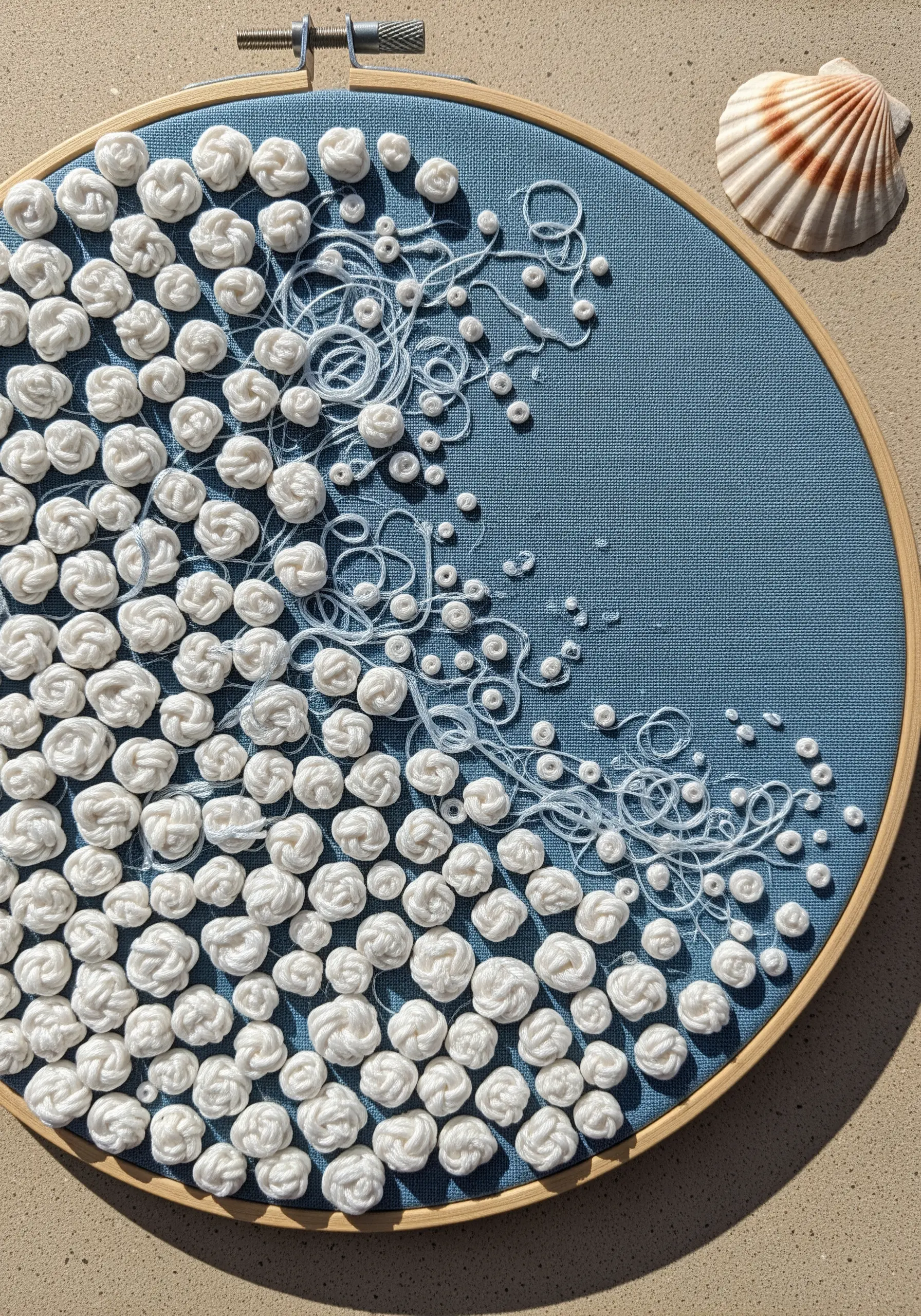 White woven wheel knots transitioning into loose threads to mimic sea foam on blue fabric.
