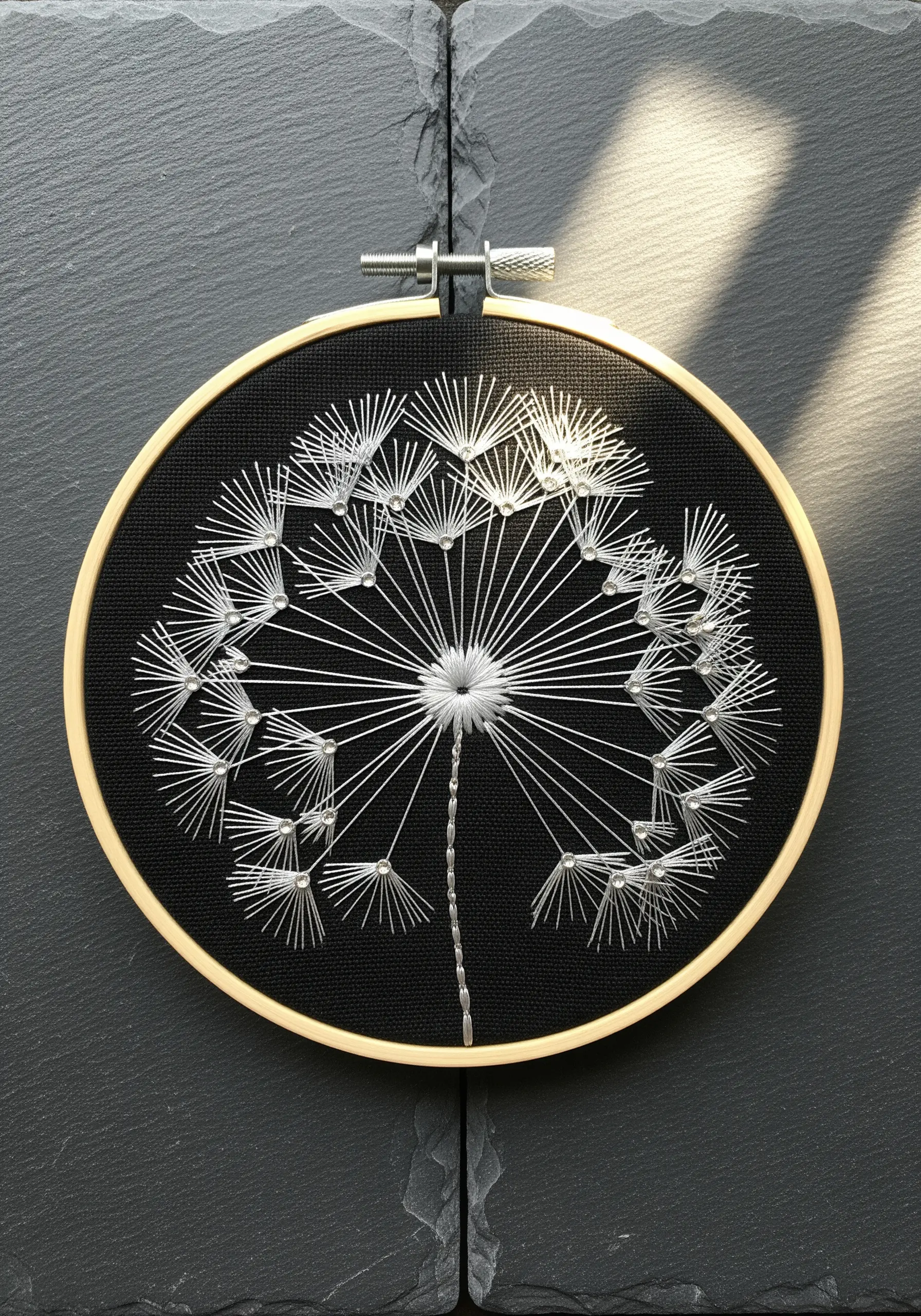 Delicate dandelion seed head stitched in white thread on black fabric.