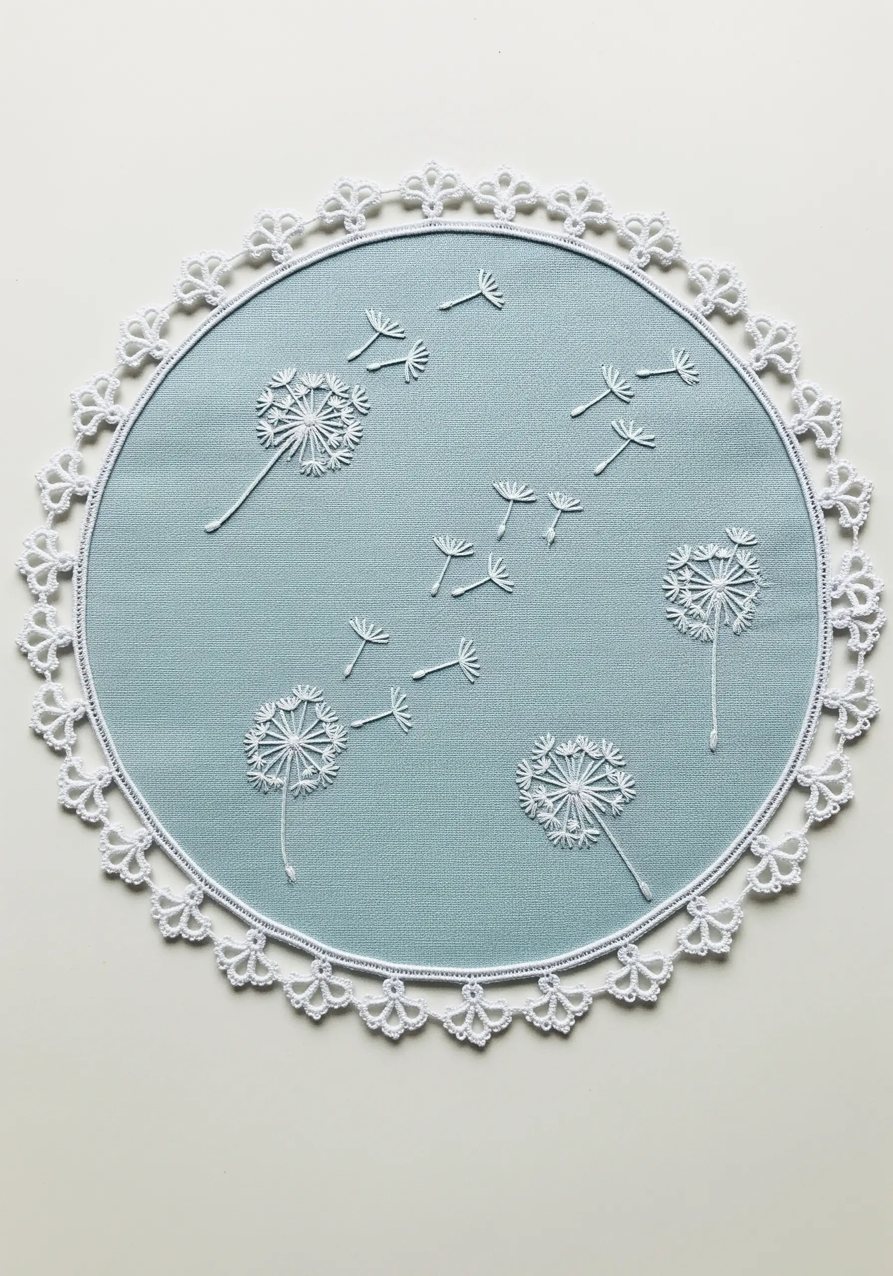 White embroidered dandelions with seeds blowing across a blue circular placemat.