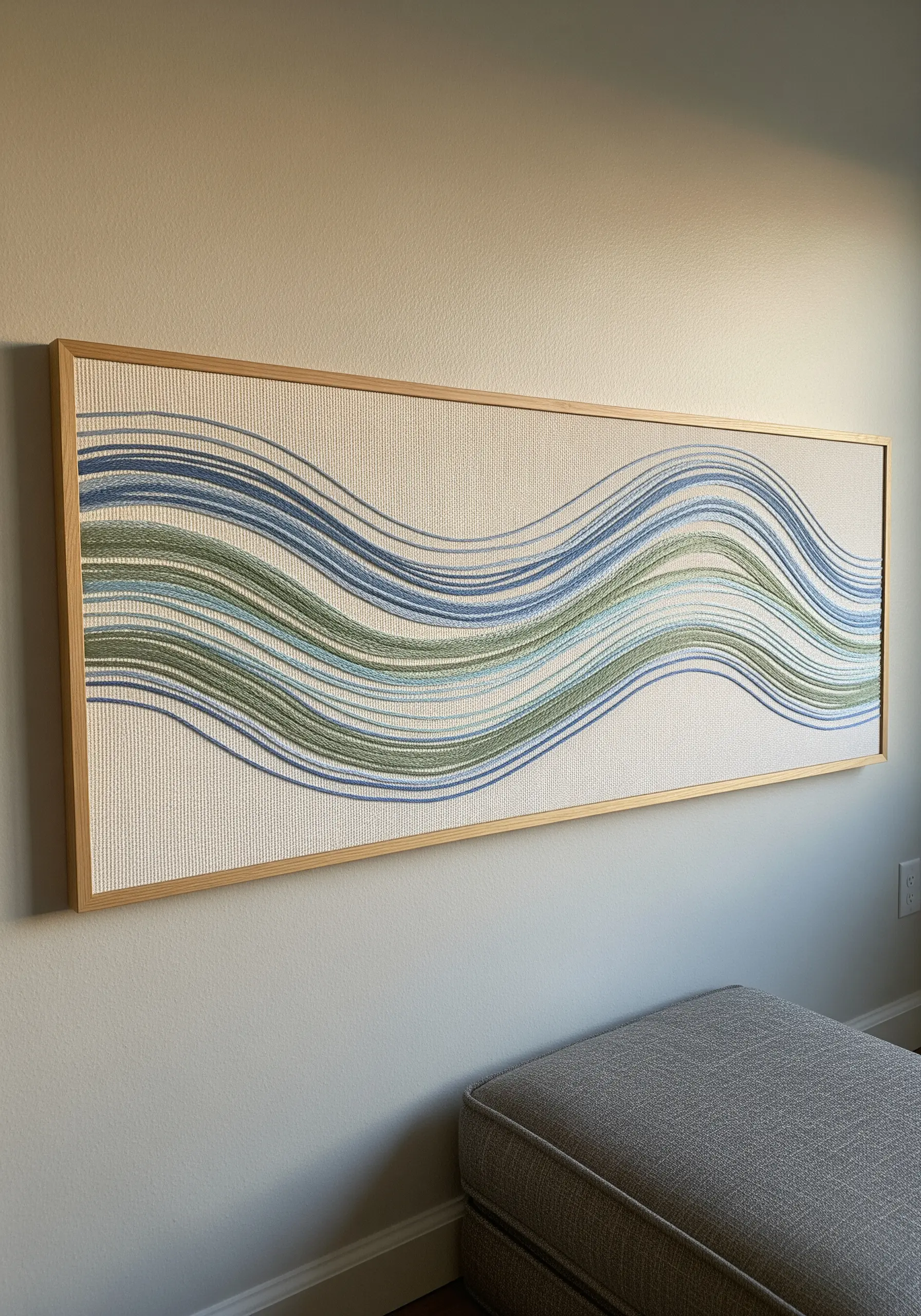 Framed horizontal embroidery of abstract waves in flowing lines of blue and green.