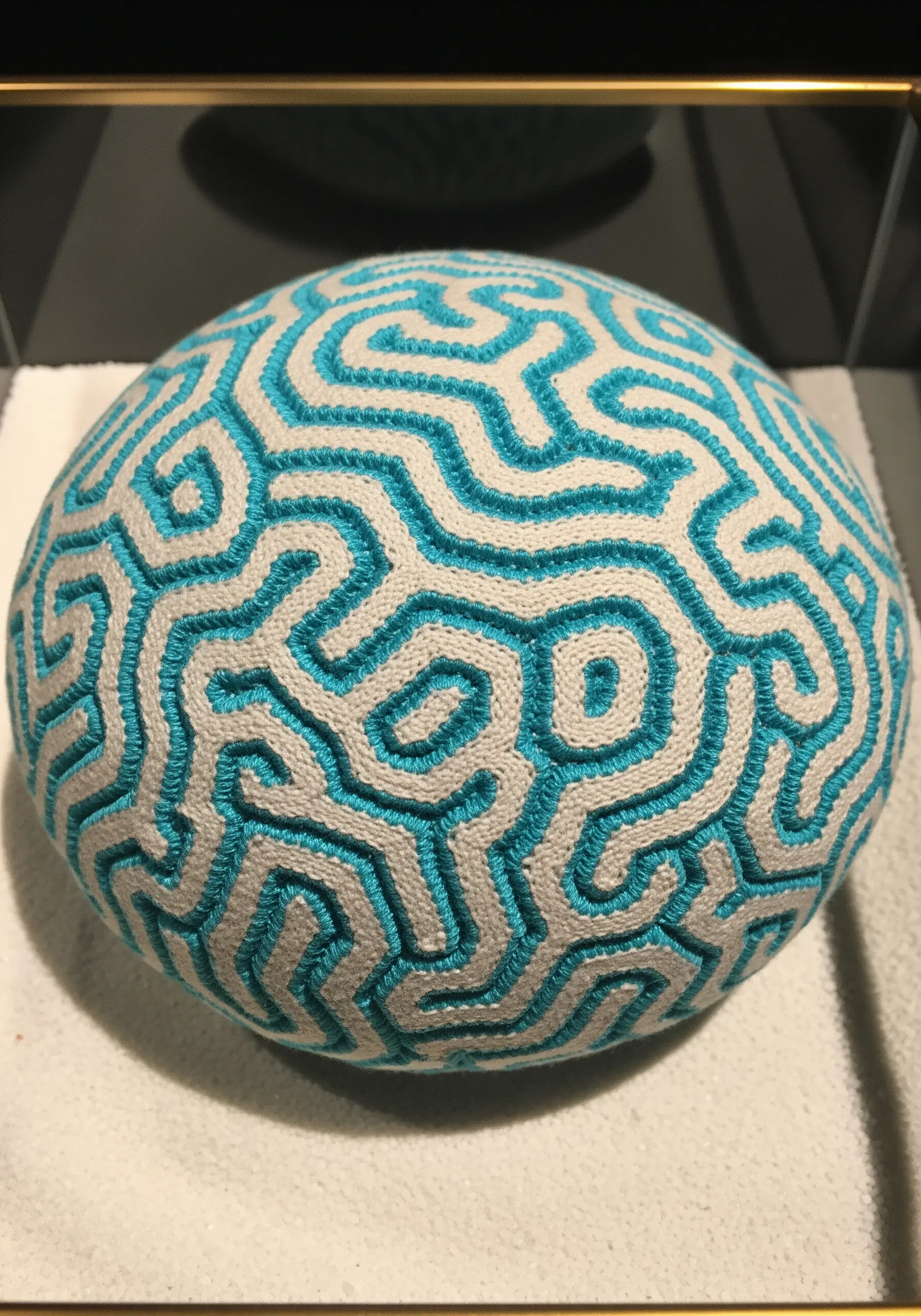 A spherical object covered in embroidery resembling a brain coral pattern.