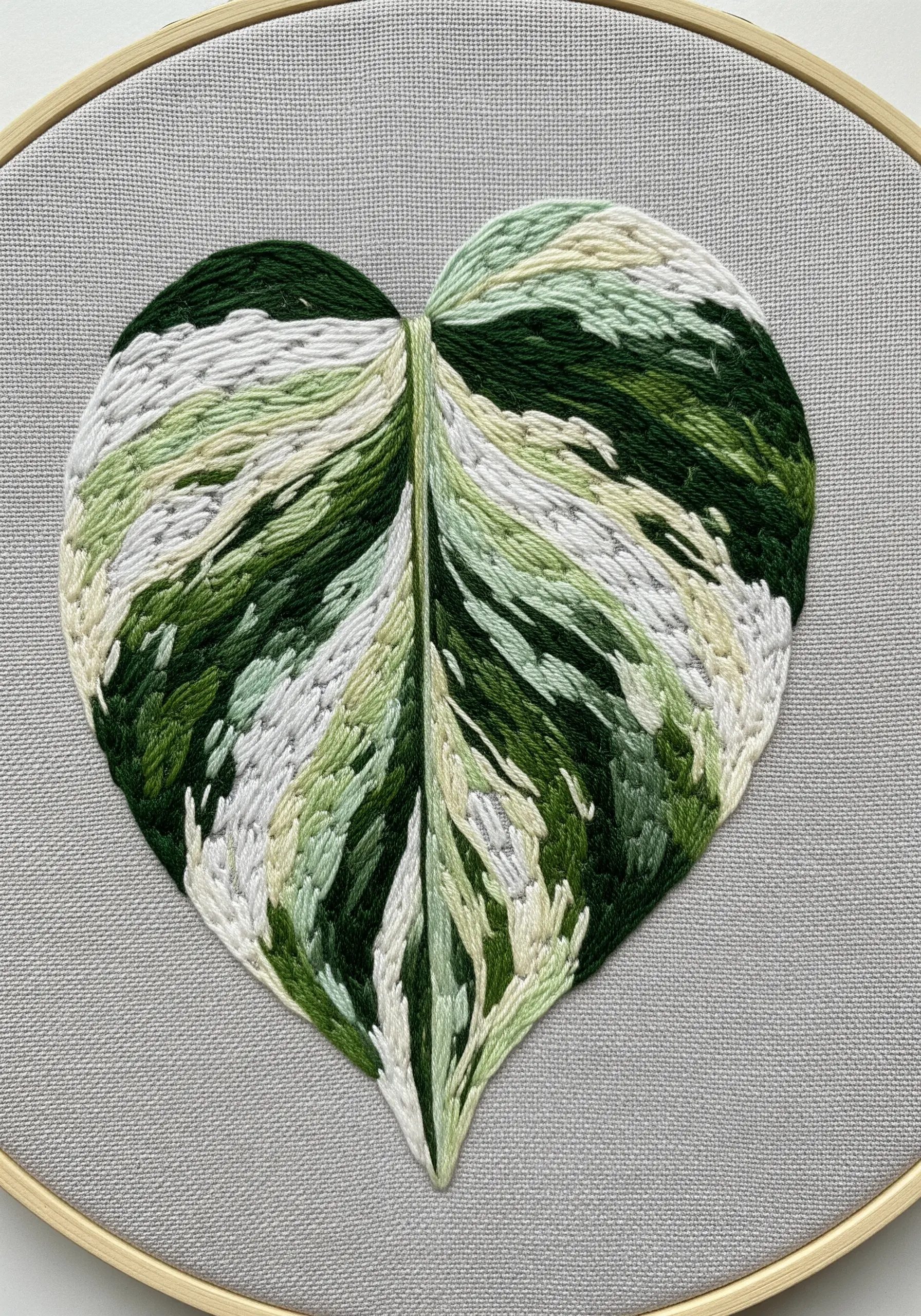 A heart-shaped variegated leaf embroidered with painterly green, cream, and white stitches.