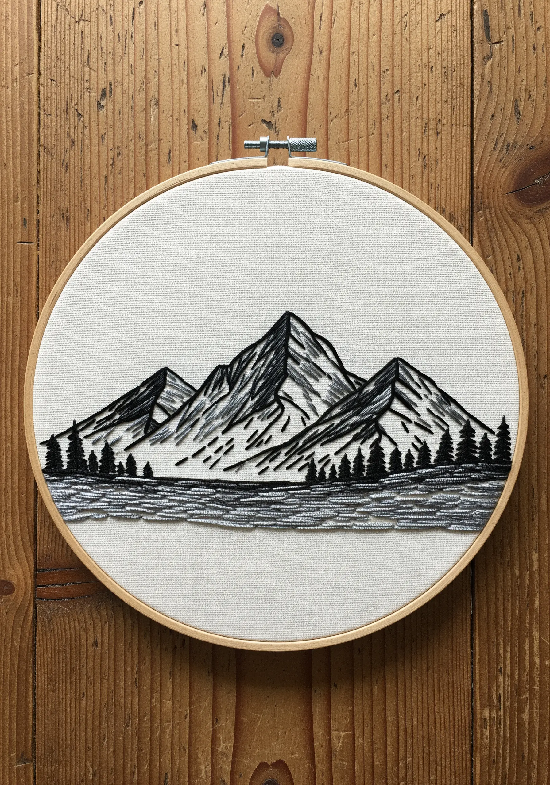 Embroidered mountain range with textured shading and smooth, reflective water in black thread.