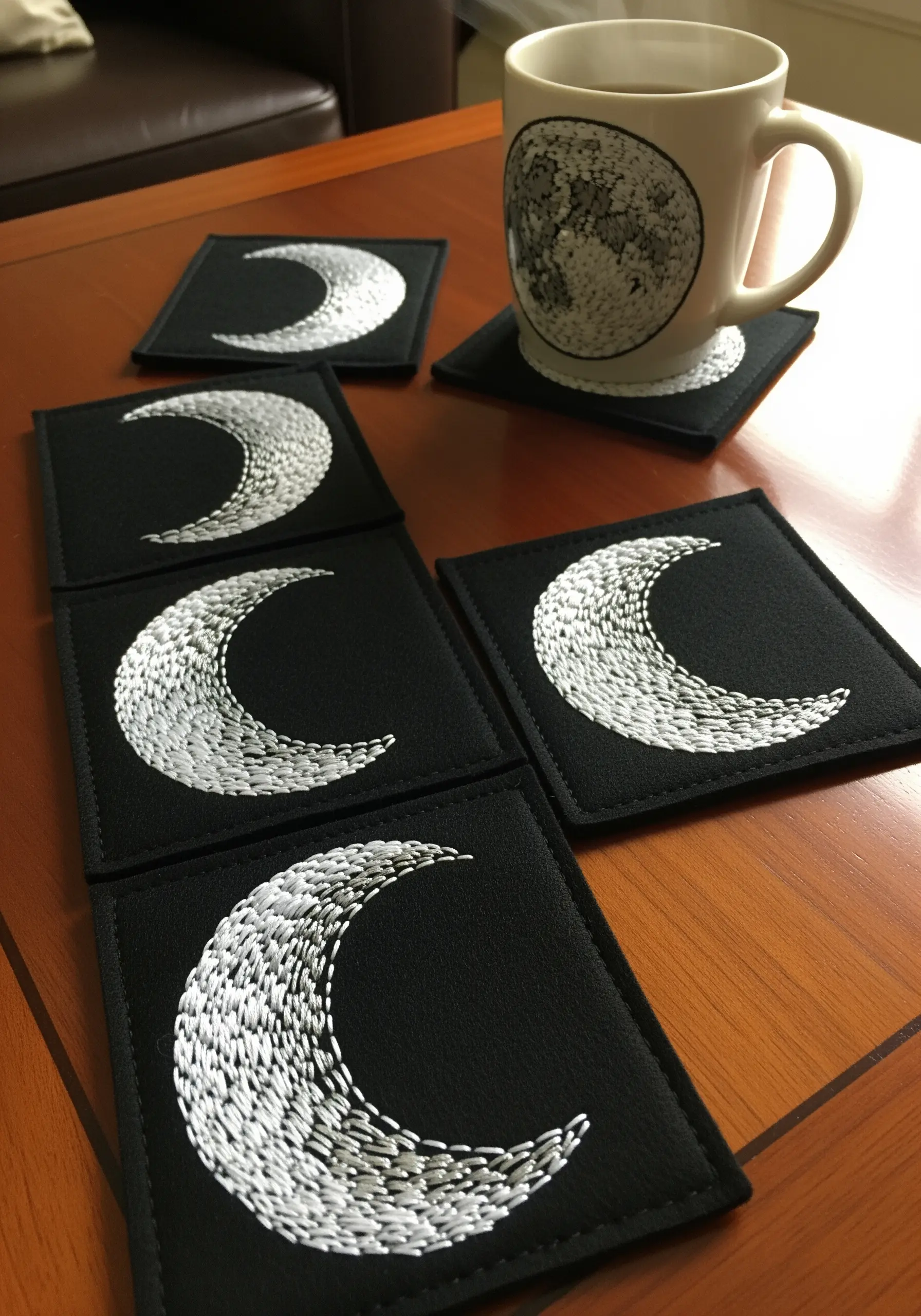 A set of black coasters, each embroidered with a crescent moon filled with textured white seed stitches.