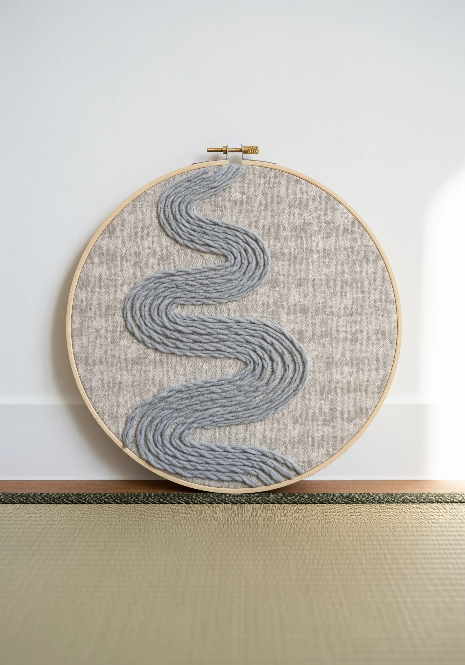 A thick, gray yarn couched onto neutral linen to form a winding river pattern.