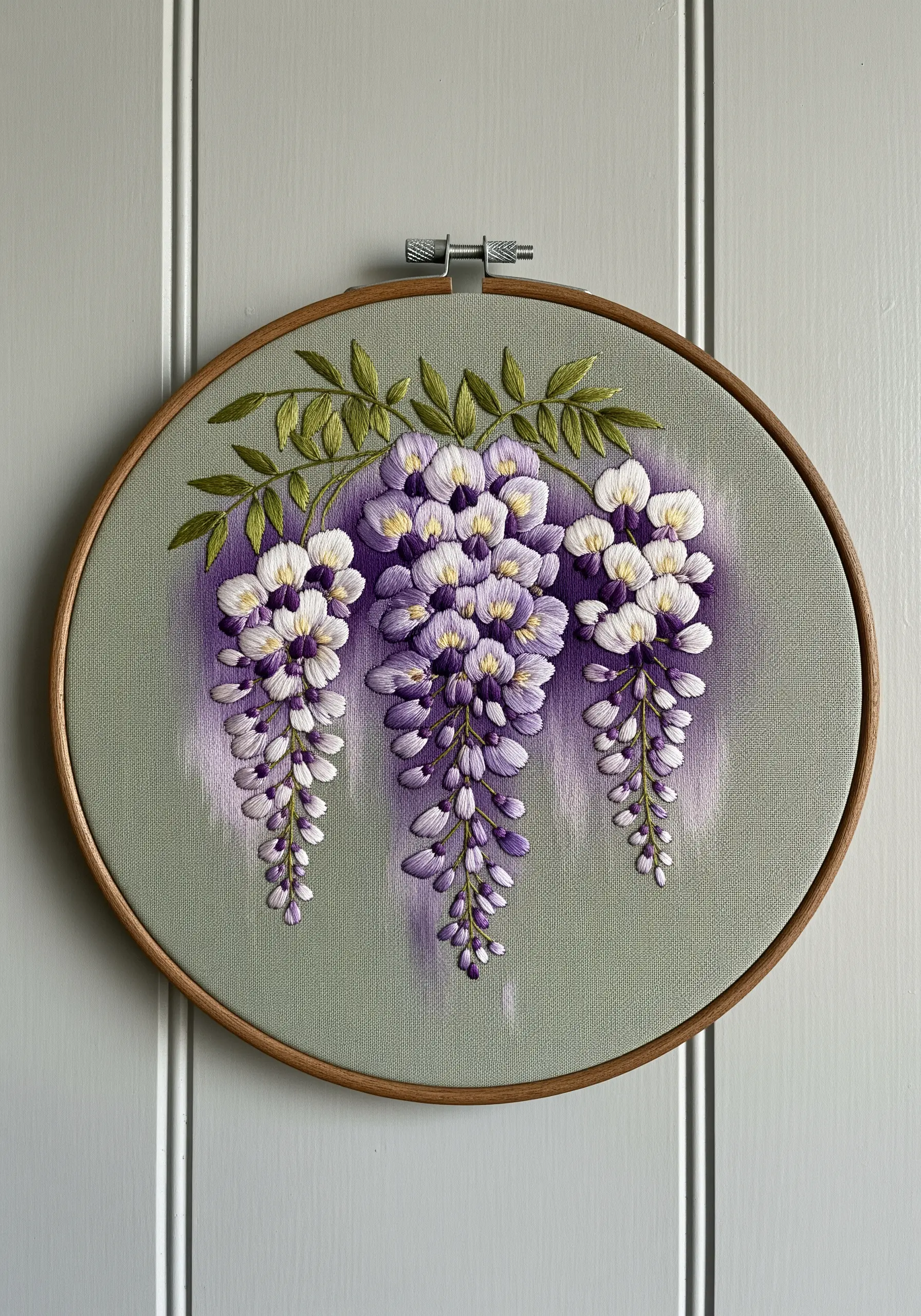 Detailed thread-painted wisteria blossoms hanging against a grey-green fabric with a purple wash.