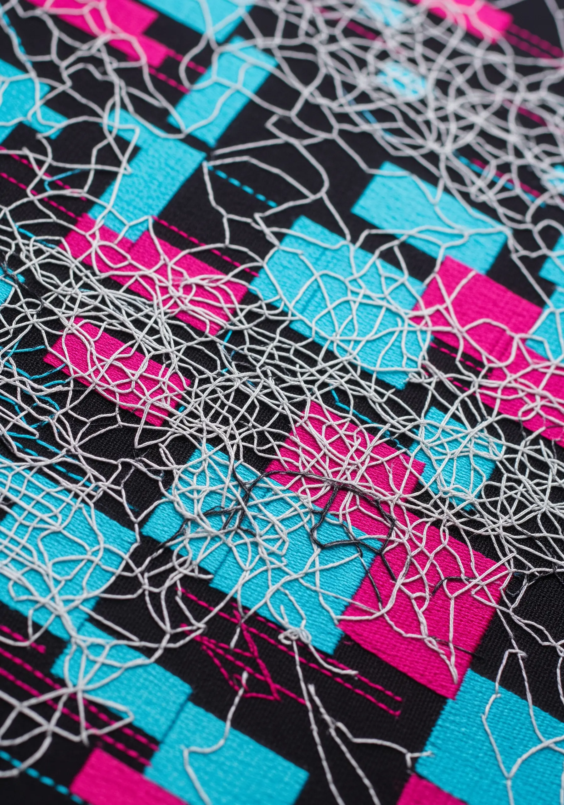 A chaotic web of white thread stitched over a geometric background of pink and blue squares