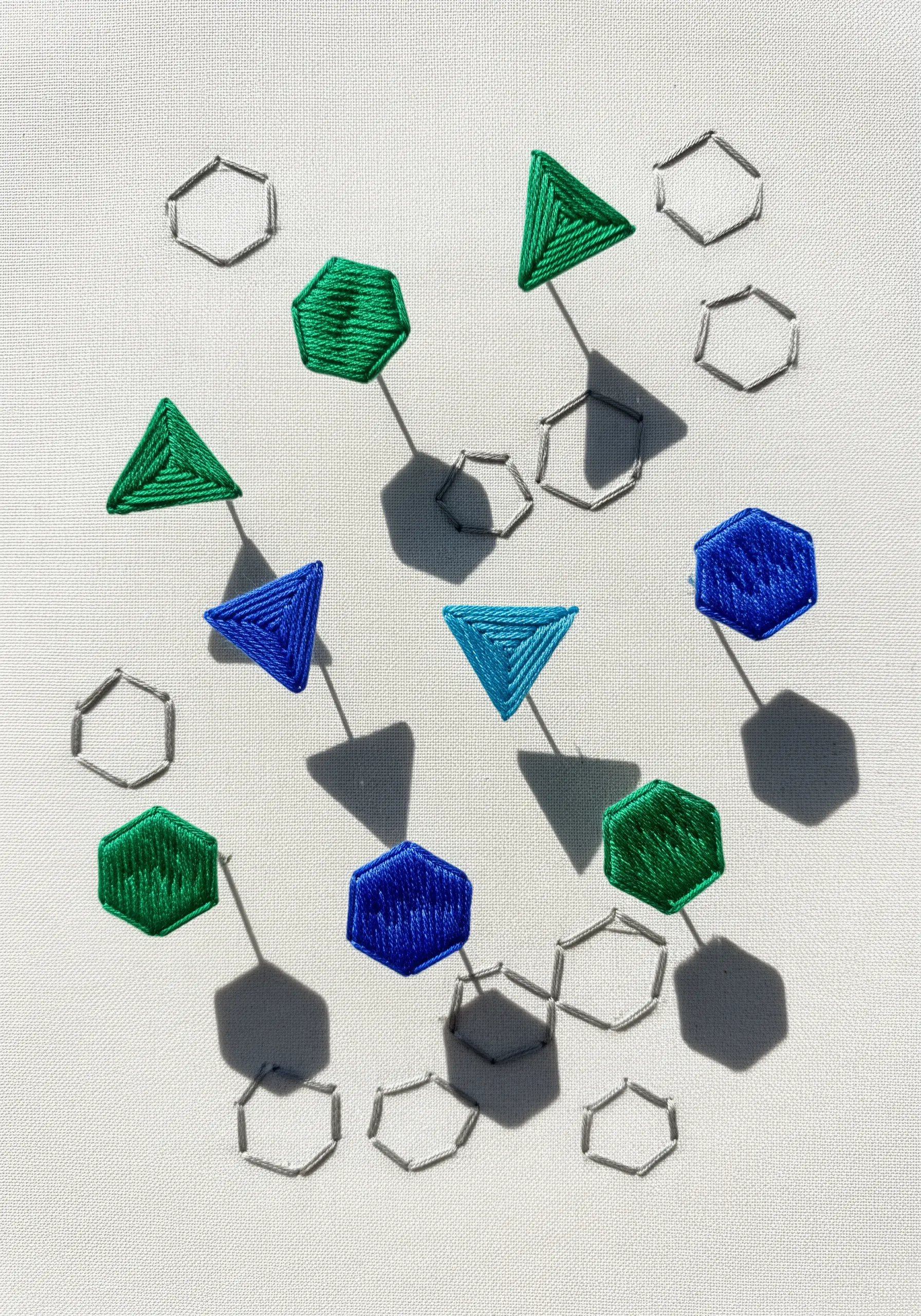 Embroidered blue and green geometric shapes with stitched gray shadows, creating a floating 3D effect.