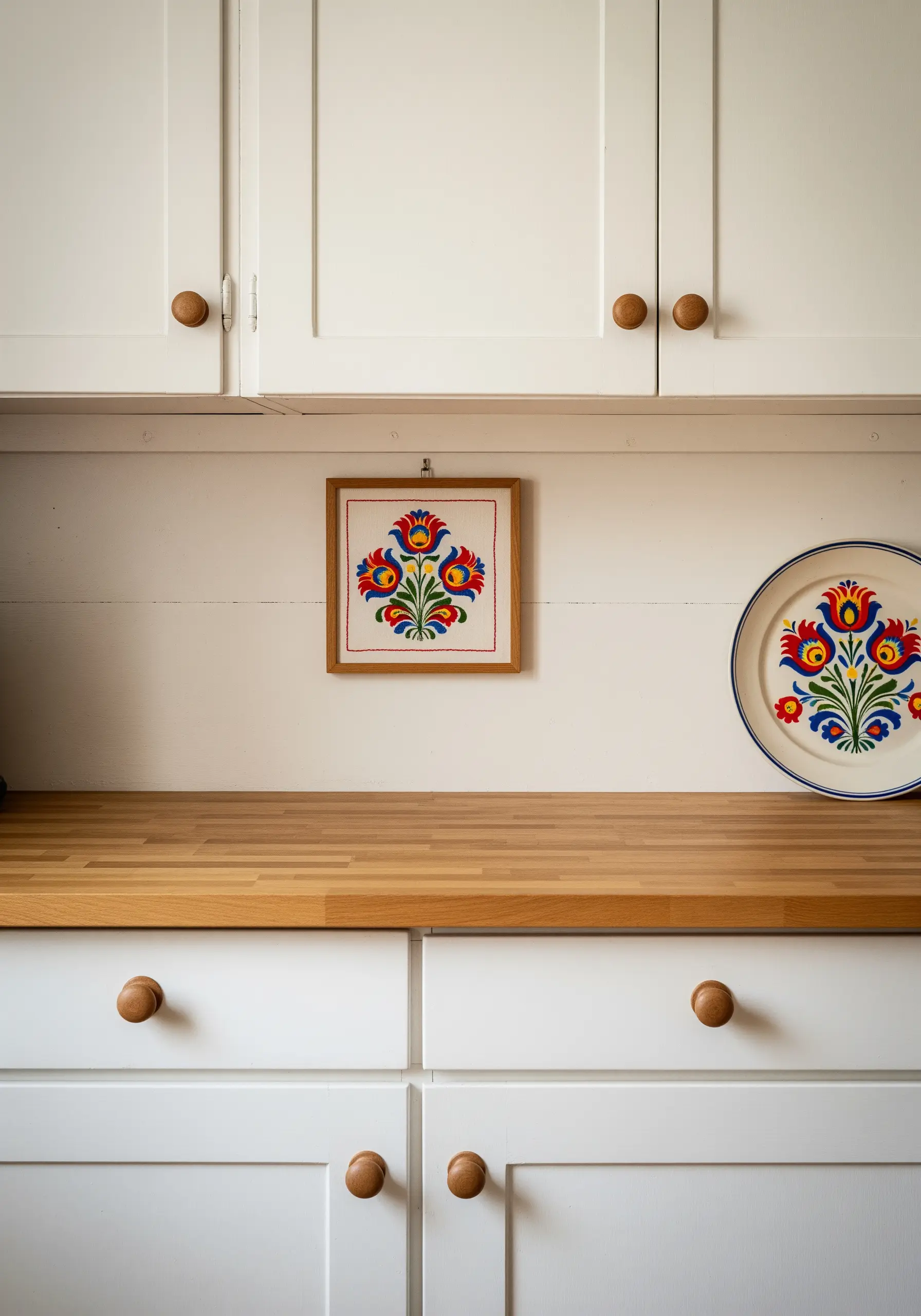 Framed folk-art floral embroidery with bold colors, next to a matching decorative plate.