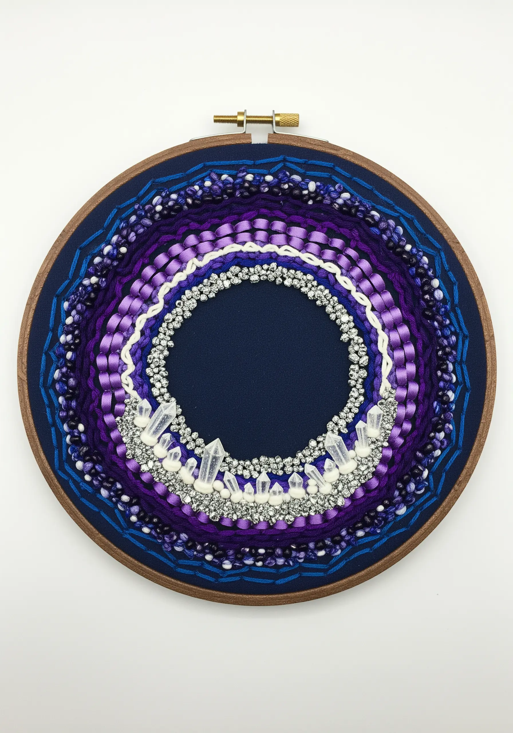 A circular, geode-inspired embroidery with purple ribbons, beads, and quartz crystals.