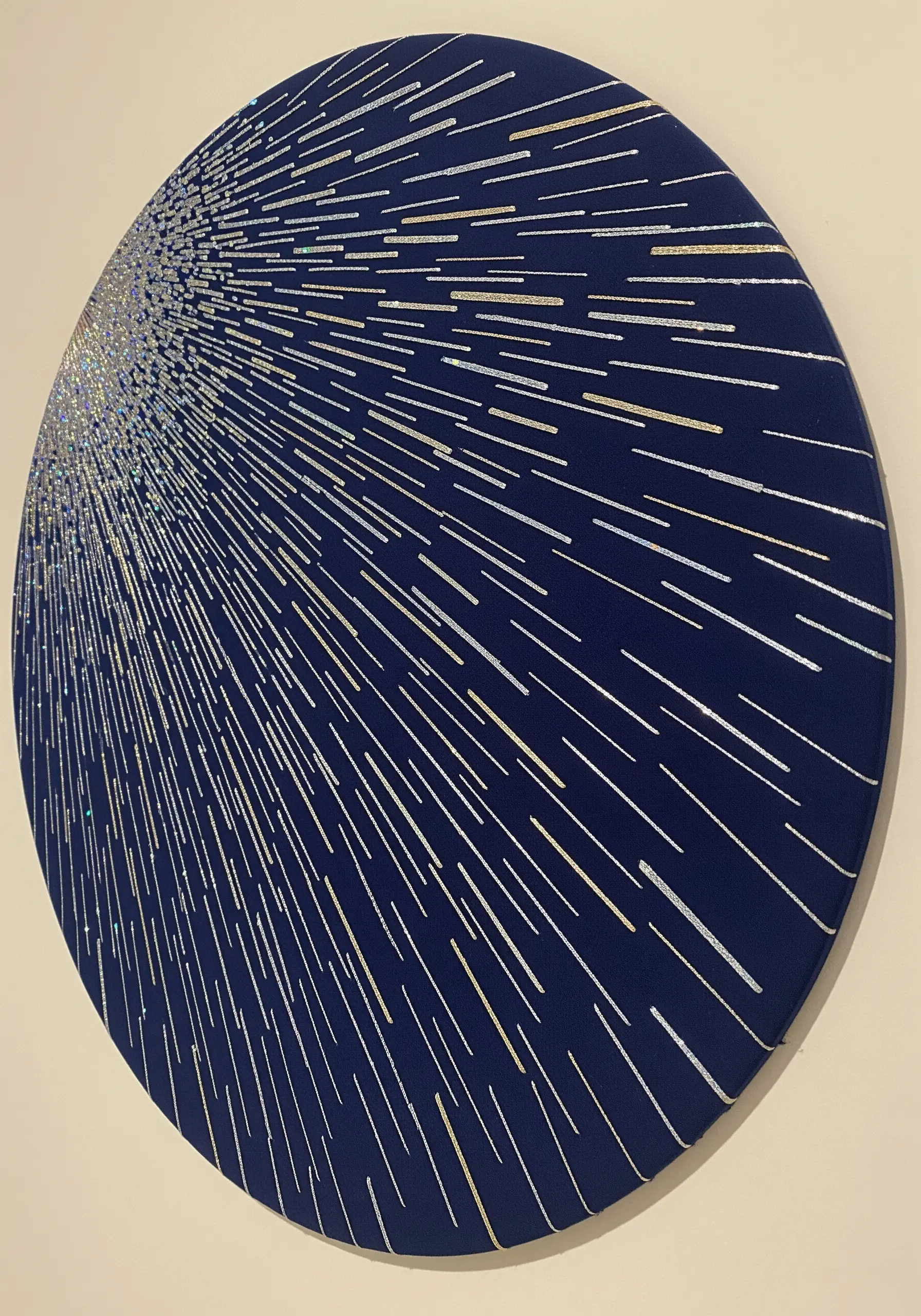A starburst effect made with radiating silver straight stitches on a round navy canvas.