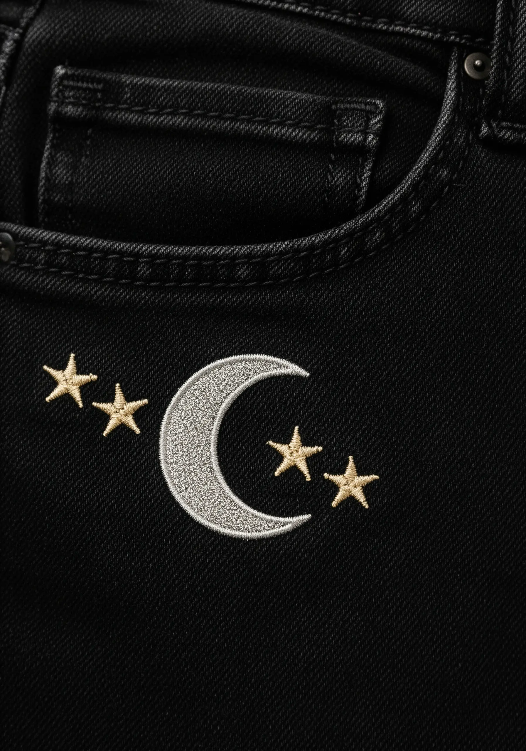 A silver crescent moon and gold stars stitched on the pocket of black jeans.