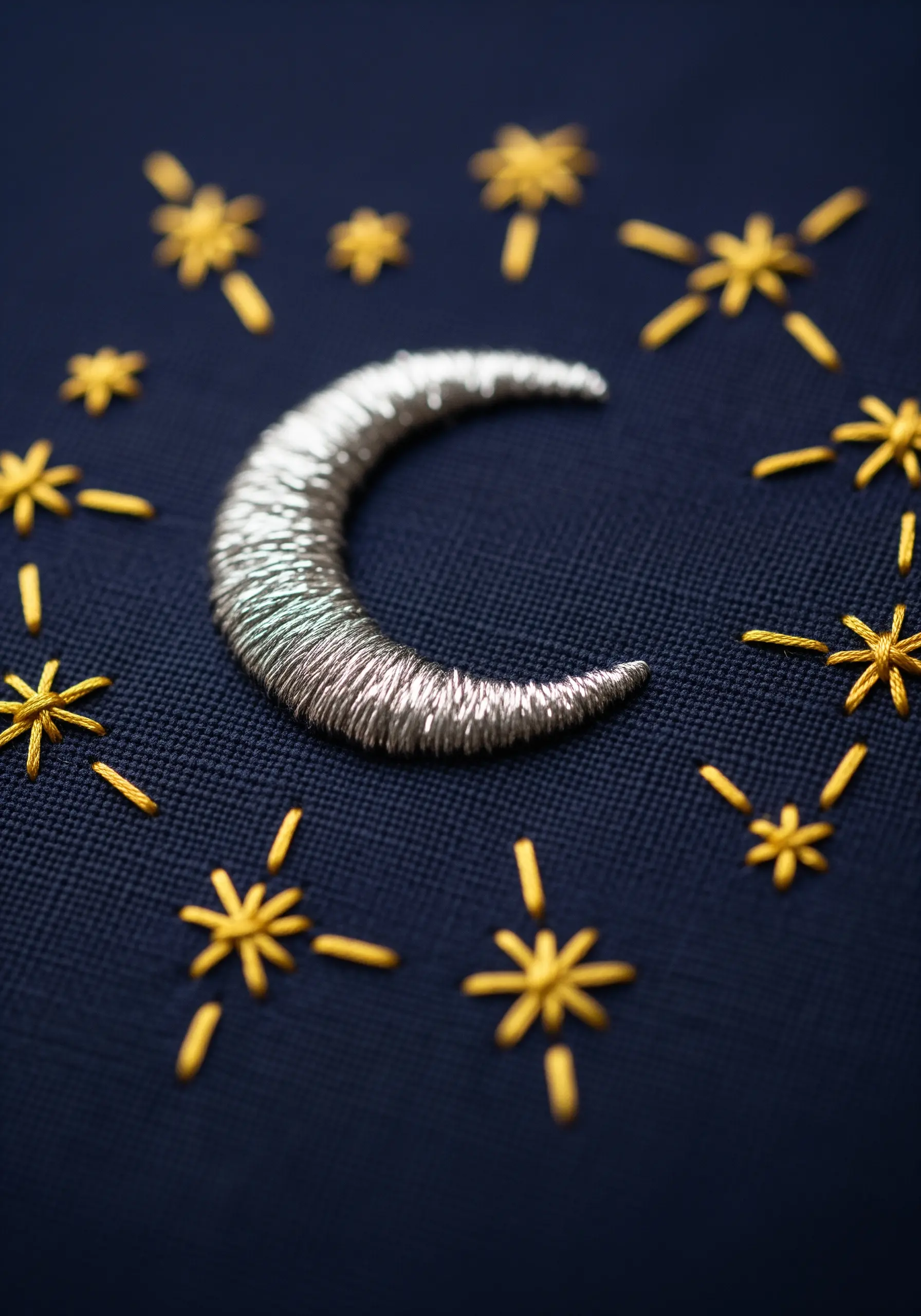 A crescent moon in shimmering silver metallic thread against a dark navy fabric.