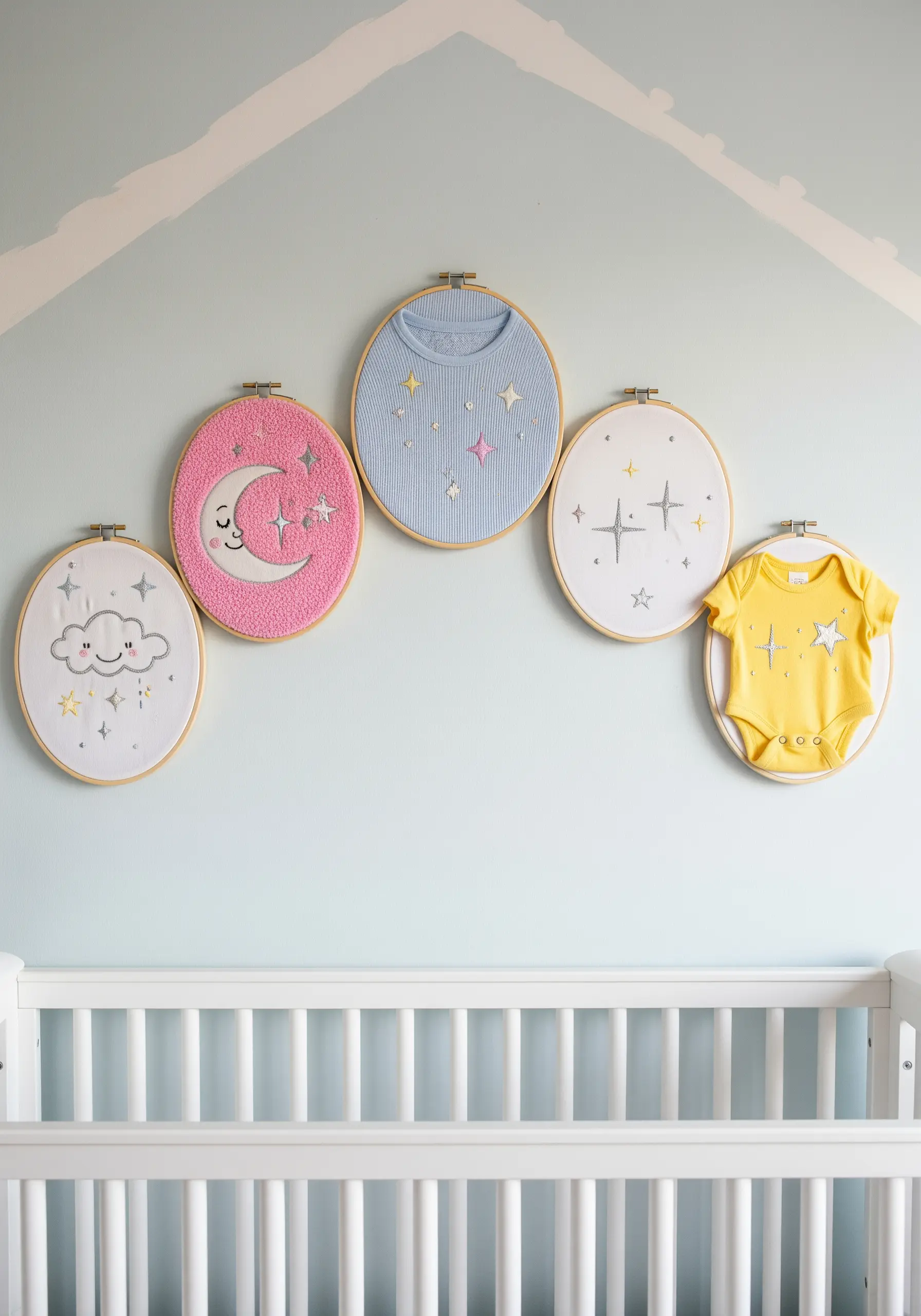 Baby clothes embroidered with clouds, stars, and moons, framed in hoops for a nursery.
