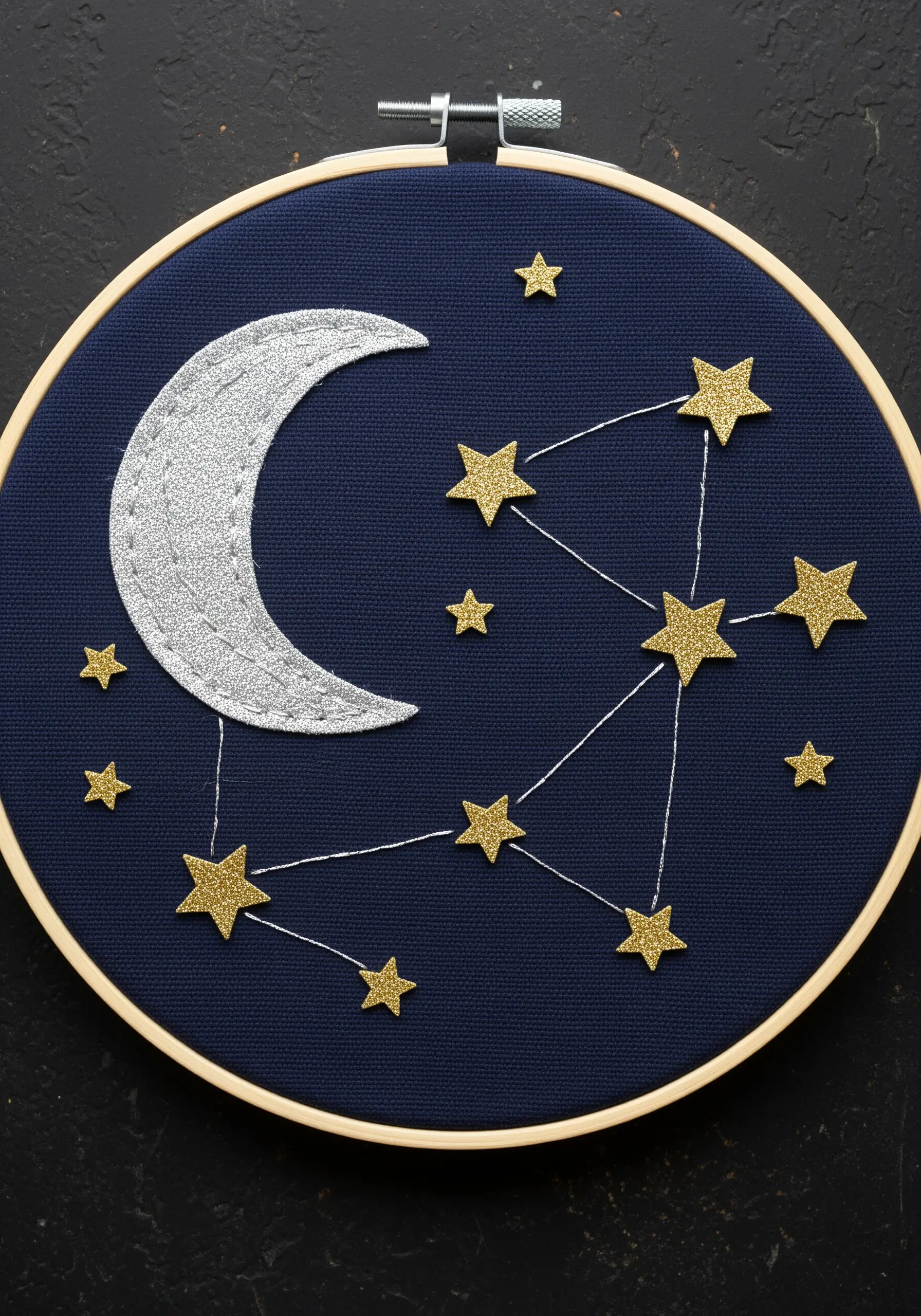 Glitter fabric moon and stars forming a constellation on dark blue fabric.