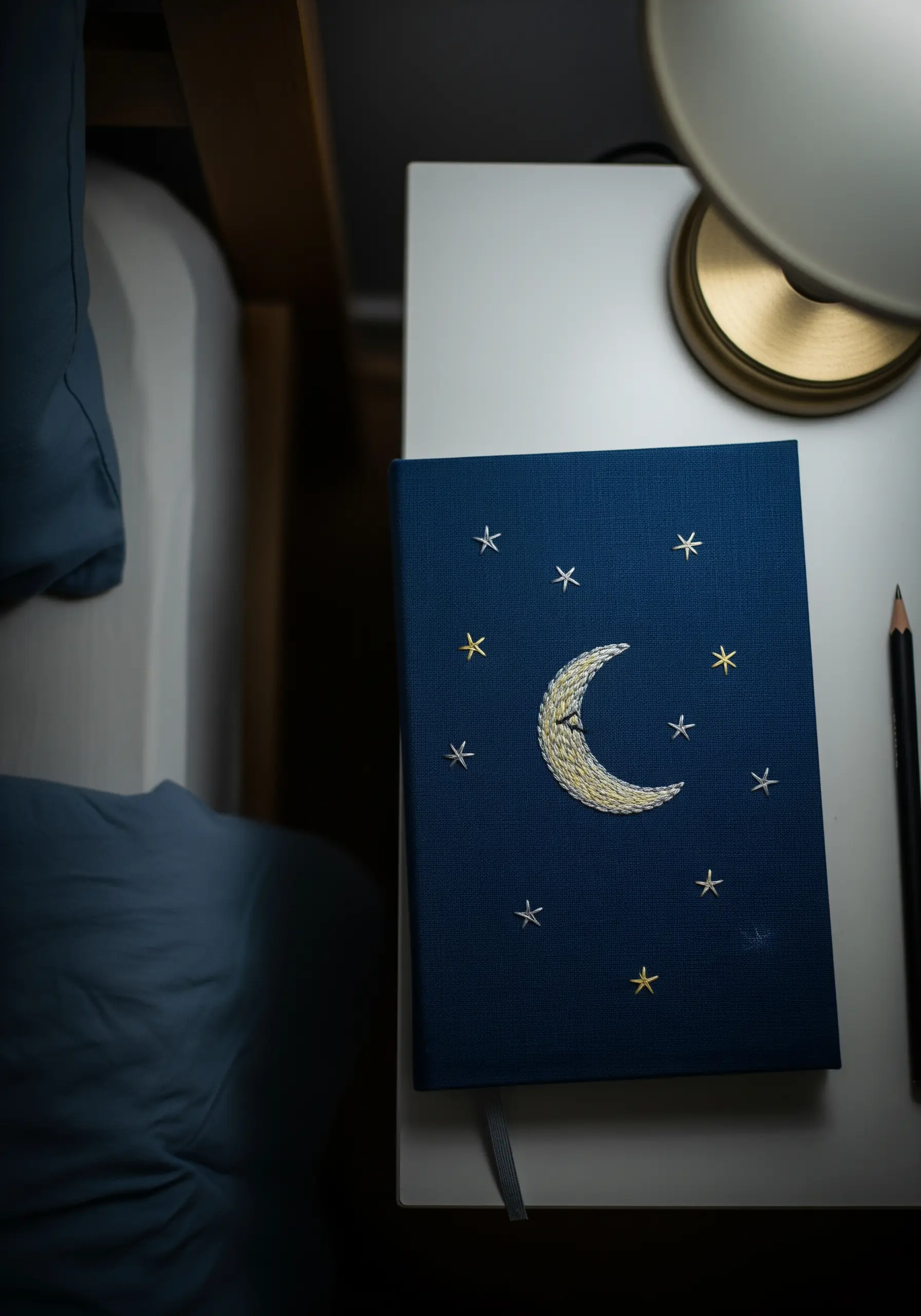 Embroidered crescent moon and stars on a dark blue cloth-bound journal cover.