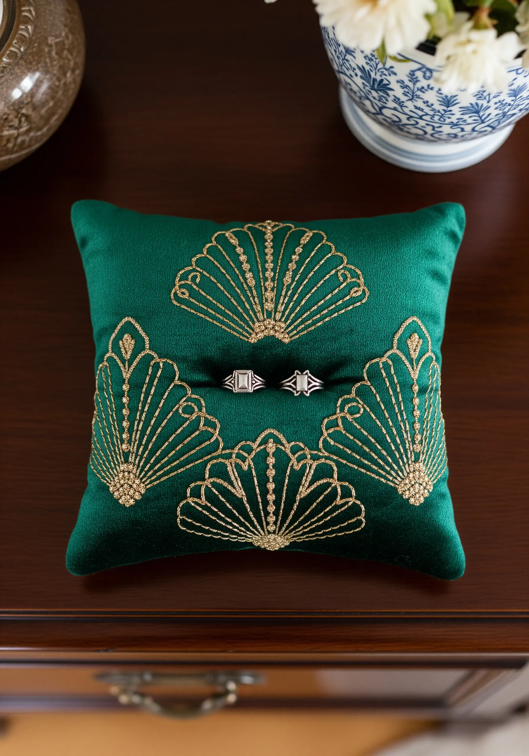 An emerald green velvet ring pillow embroidered with a geometric Art Deco fan design in gold thread.