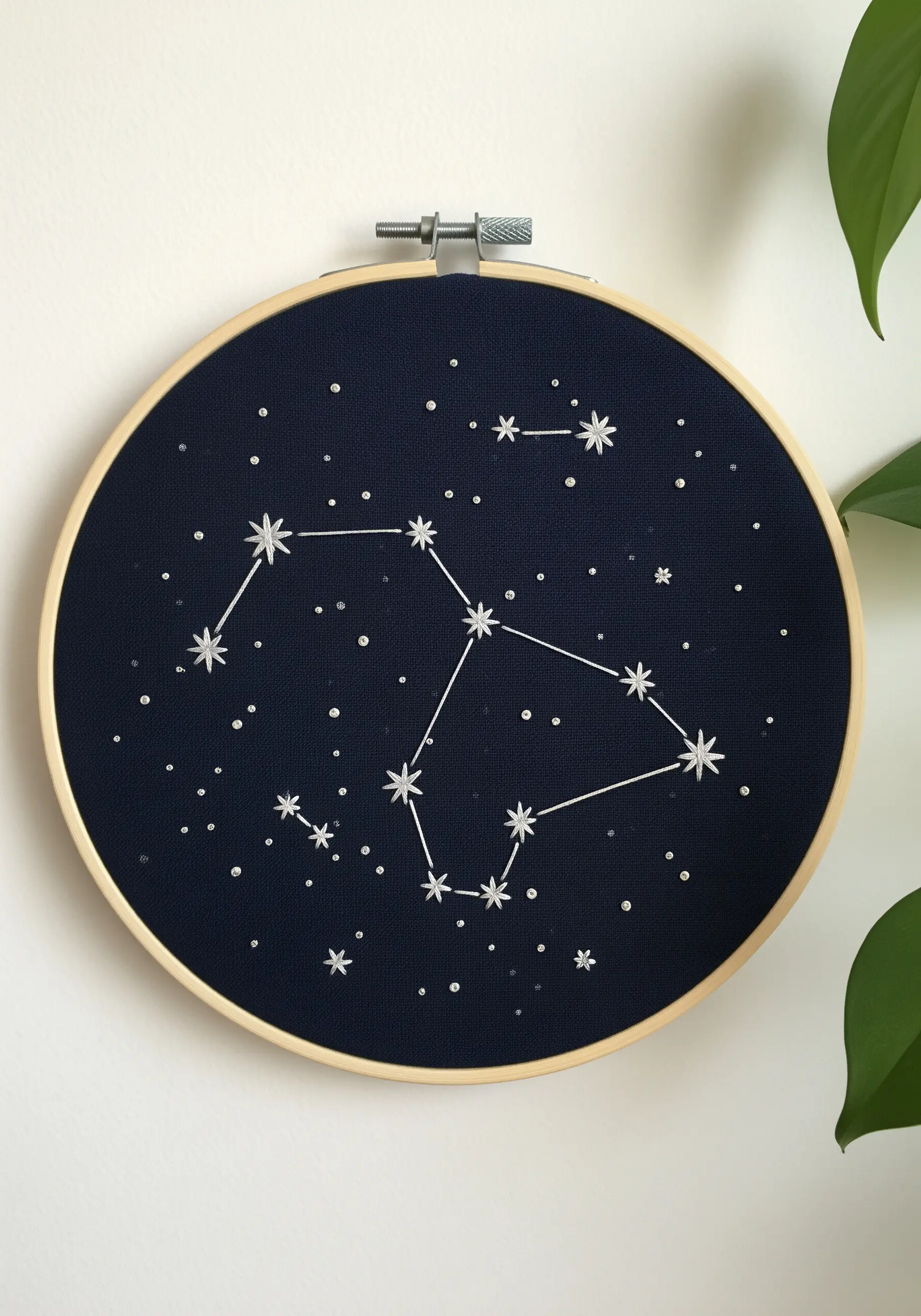 A zodiac constellation embroidered in white thread on dark navy fabric in a wooden hoop.