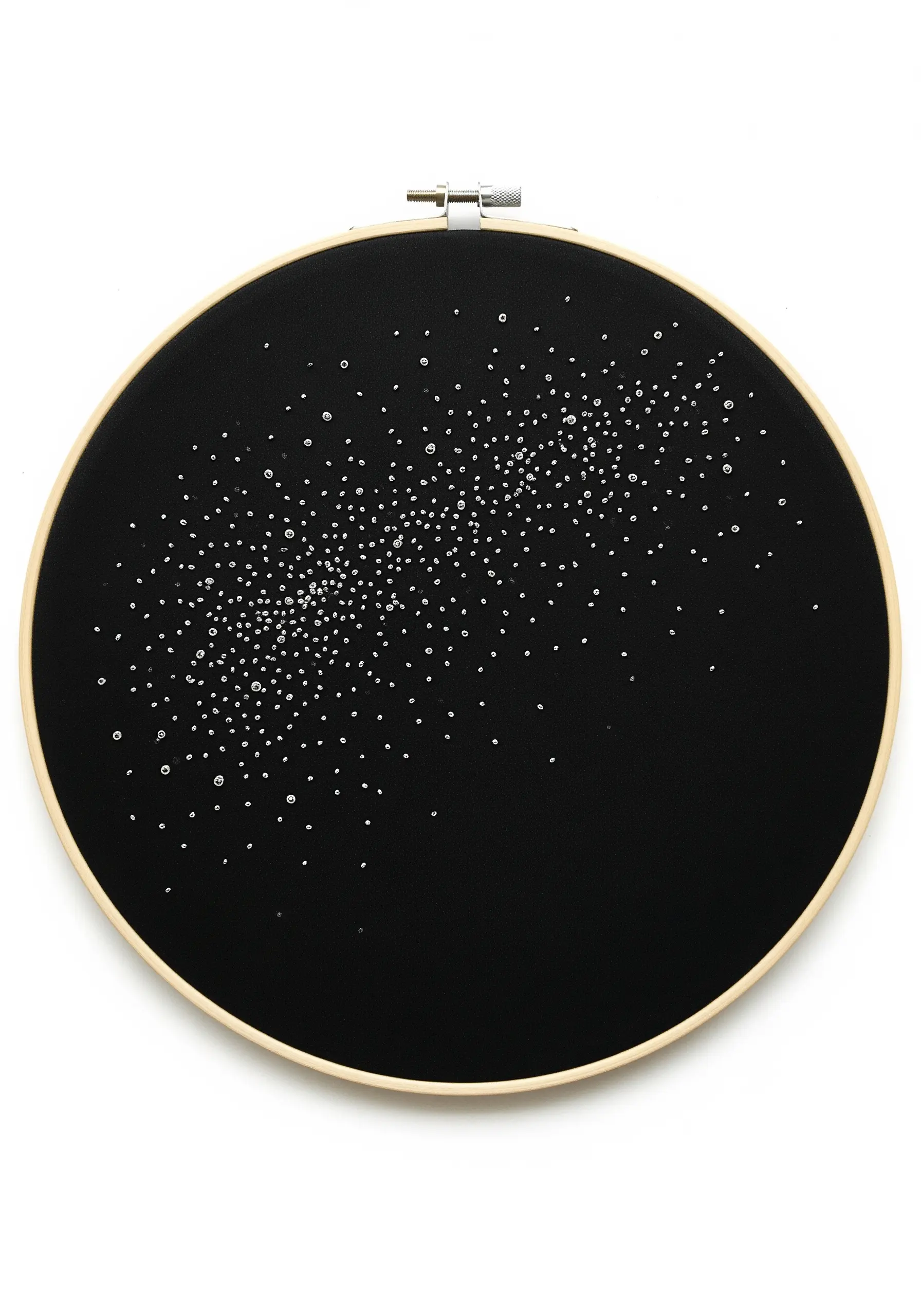 Embroidery hoop with a sweep of white French knots on black fabric, resembling a galaxy.