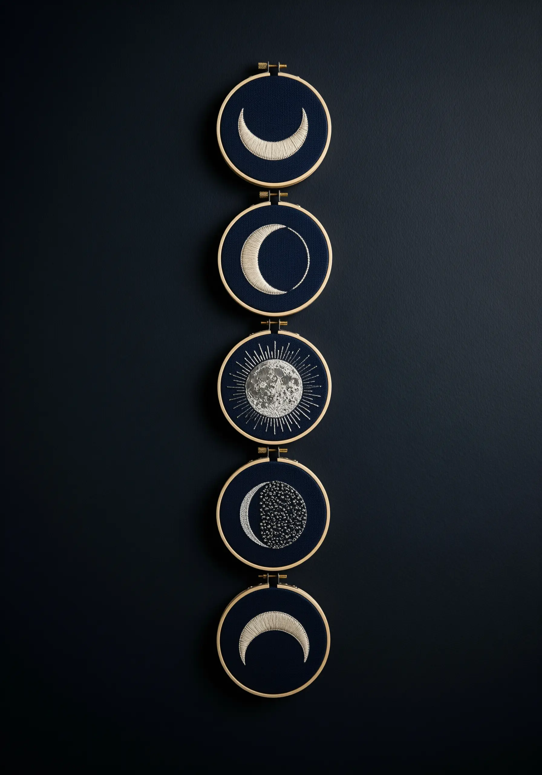 A series of five embroidery hoops showing the phases of the moon on dark blue fabric.