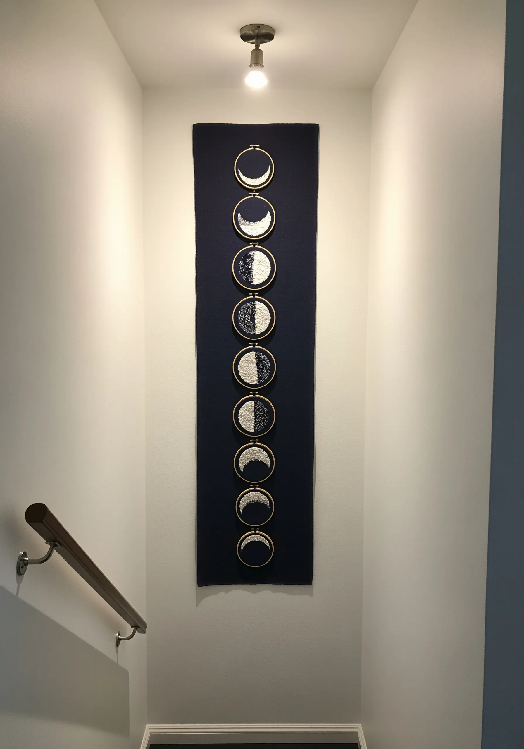 A long, vertical black fabric hanging with a series of small hoops depicting the phases of the moon.
