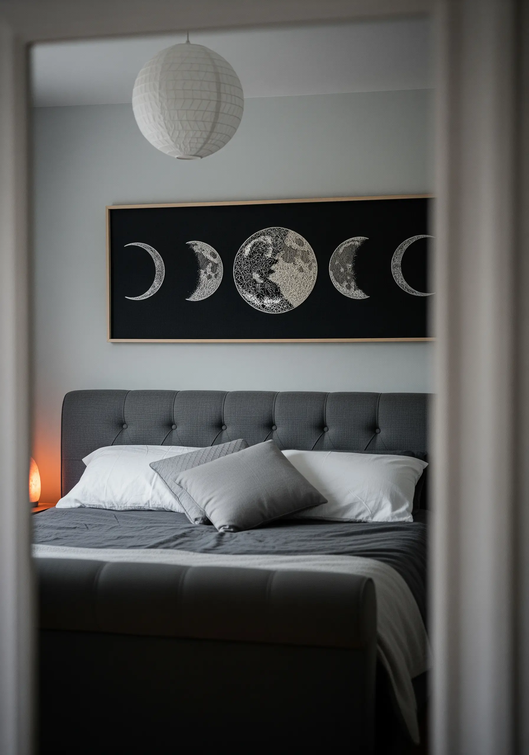 A rectangular framed embroidery of the moon phases on a black background, using white textural stitches.
