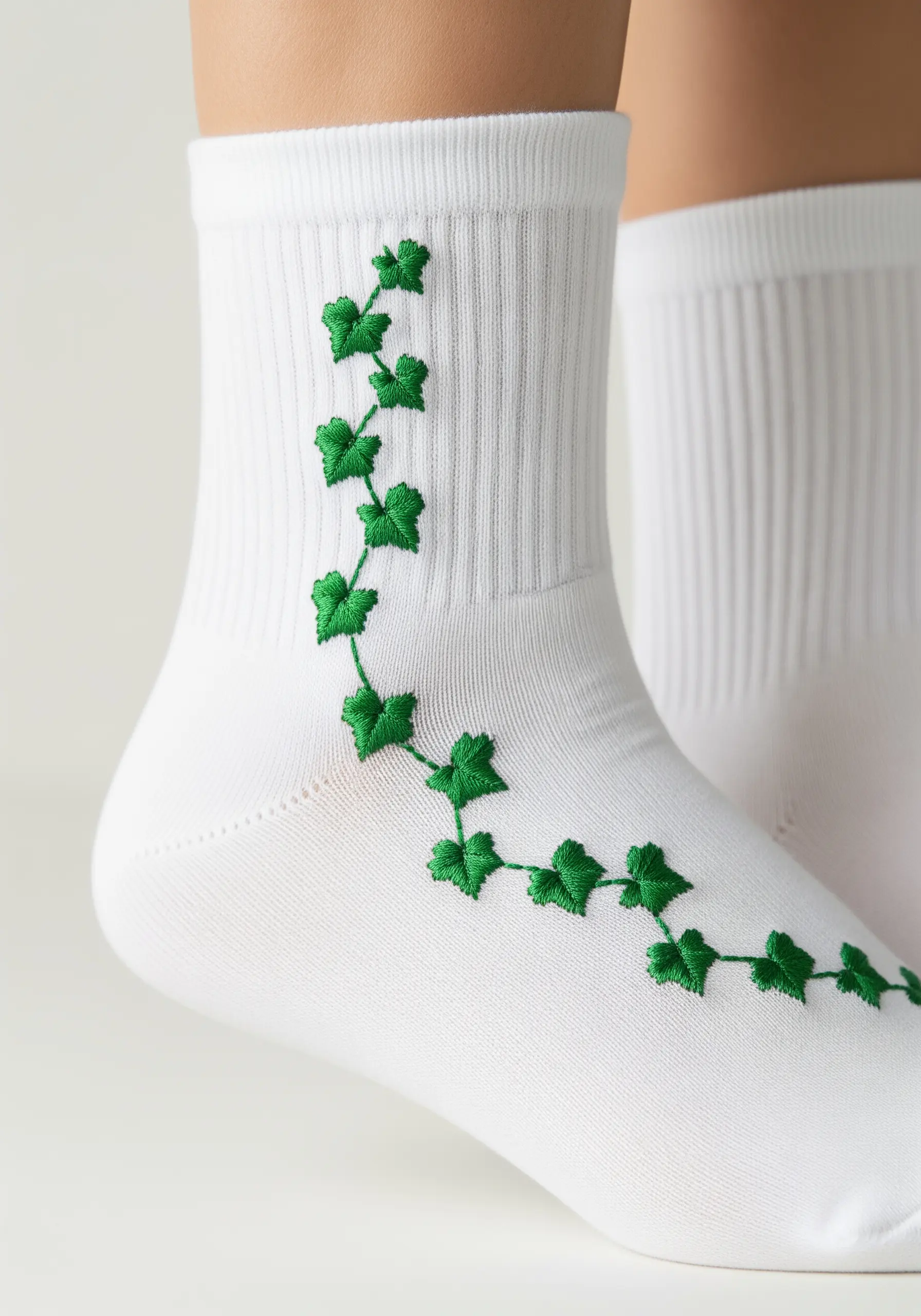 A climbing ivy vine with green leaves embroidered up the side of a white sock.