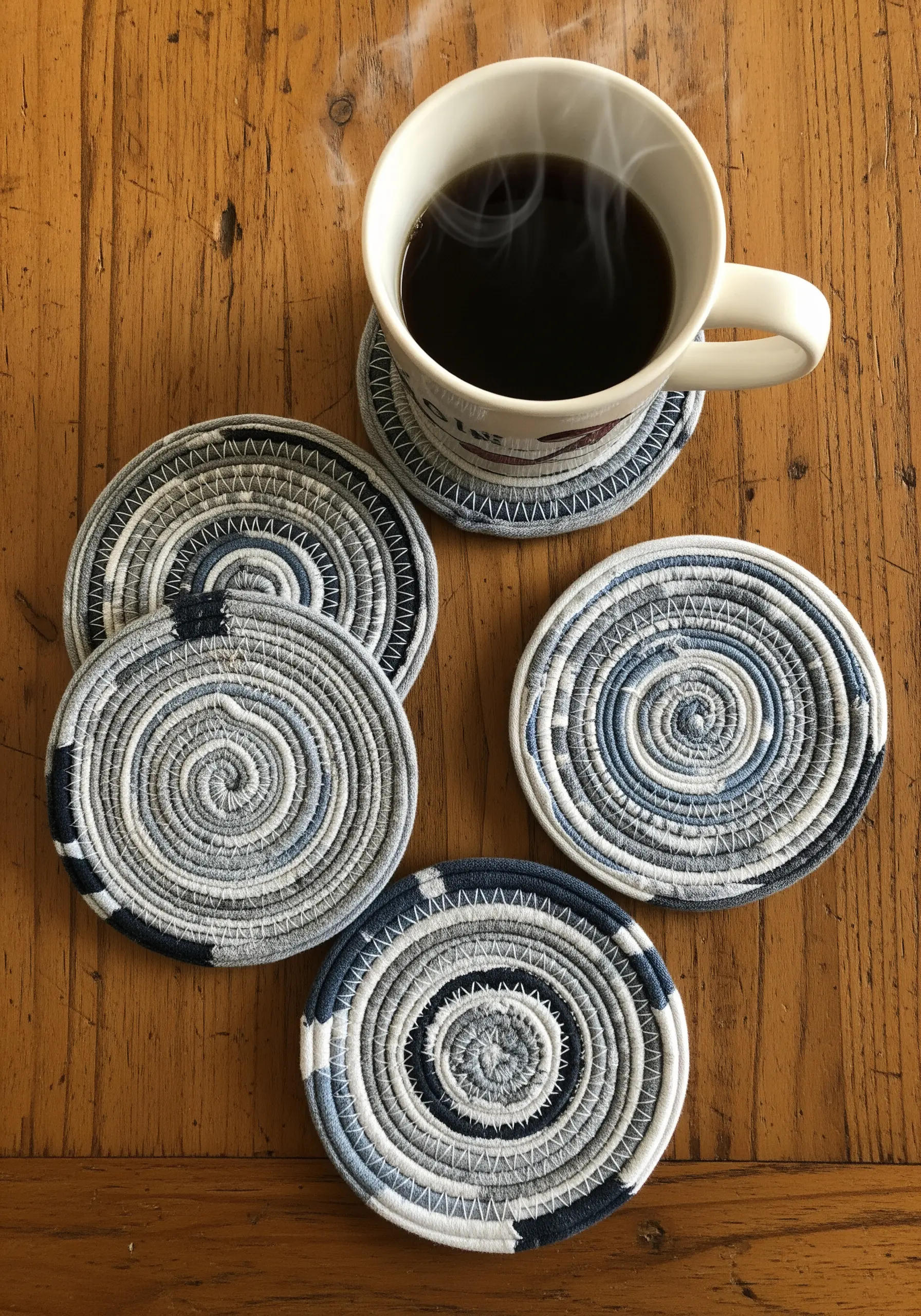 A set of five round coasters made from coiled strips of blue and white fabric.