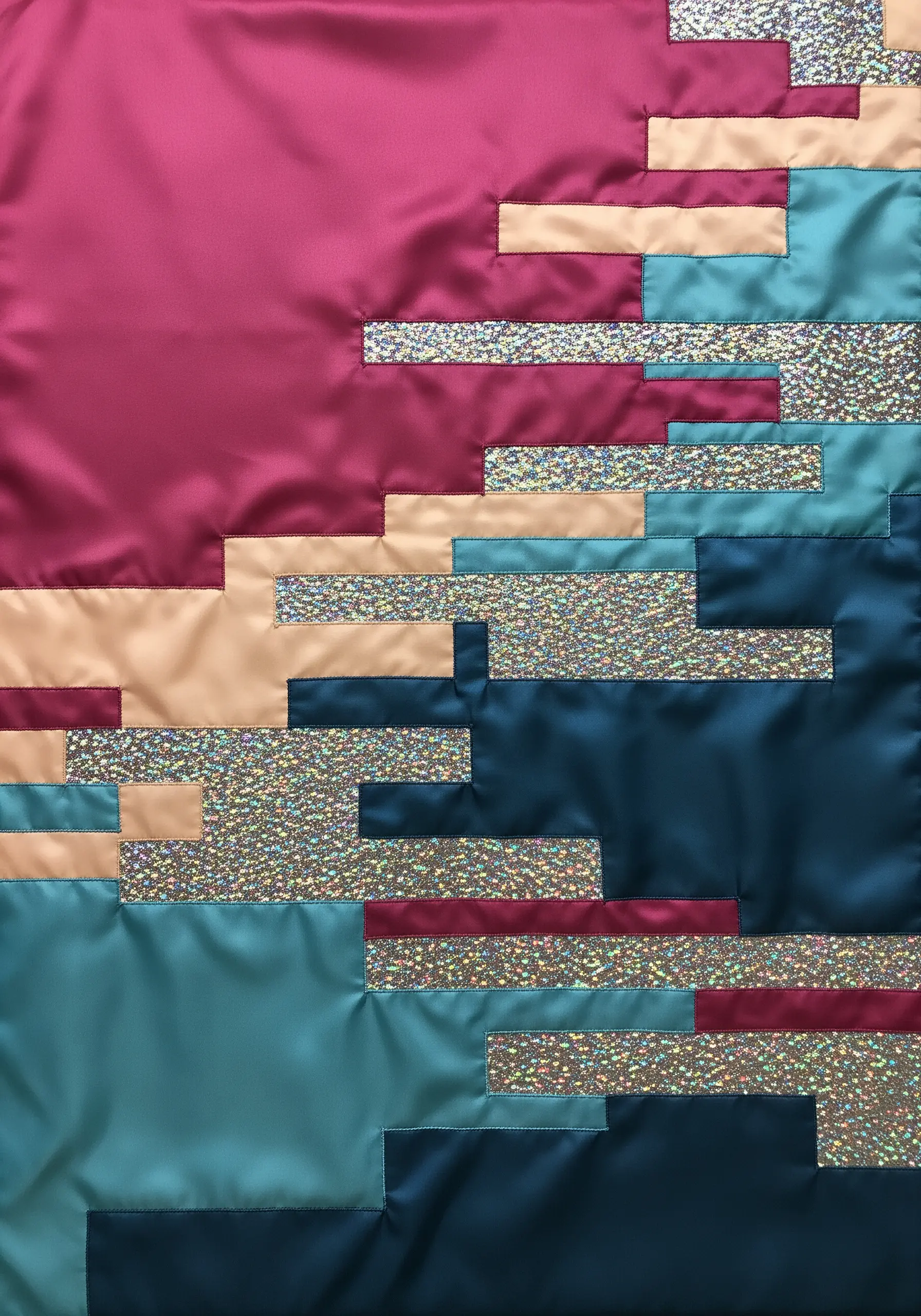 An abstract, color-blocked fabric collage using satin and glittery materials.