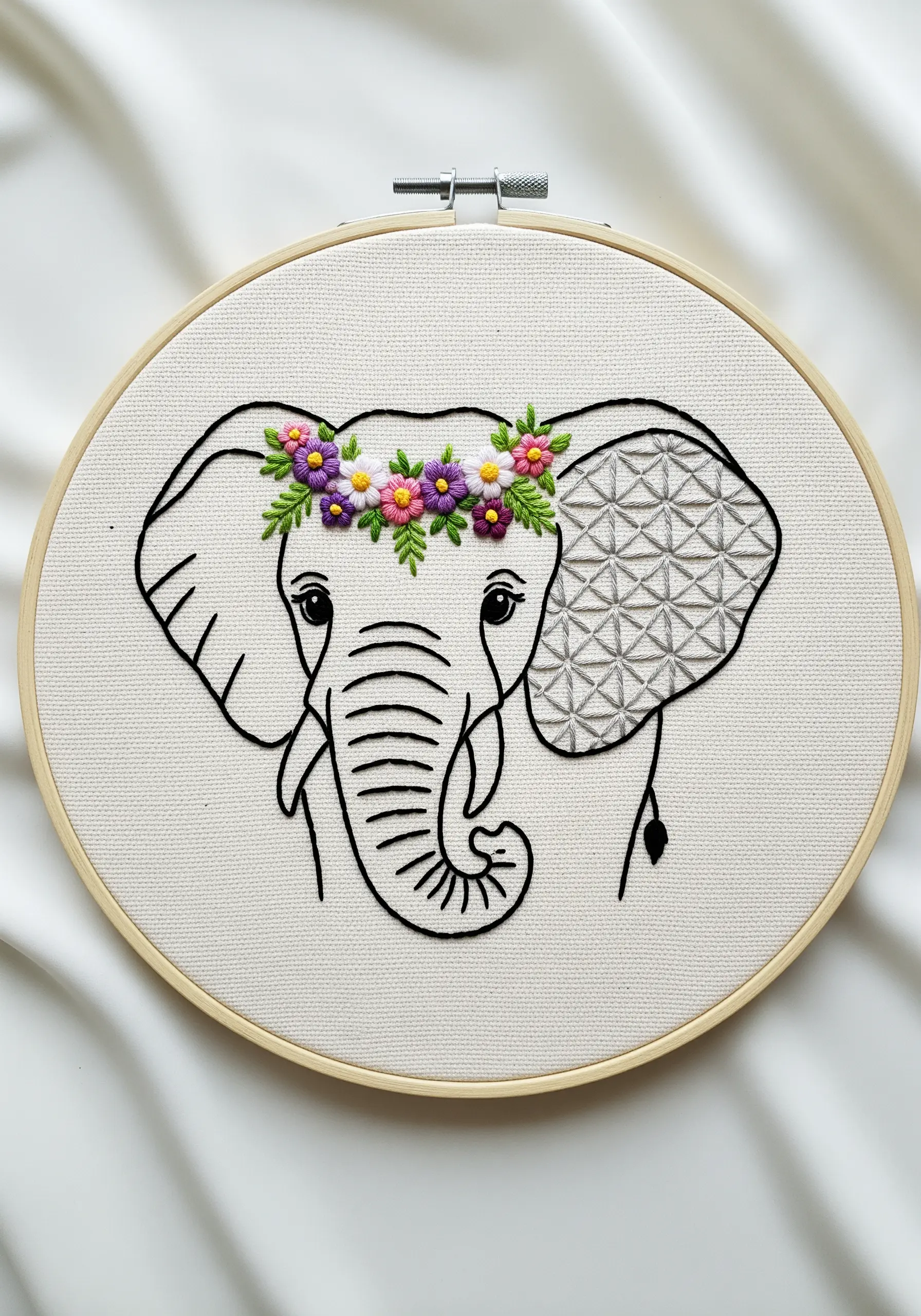 Line art embroidery of an elephant with a colorful floral crown and a geometric-filled ear.