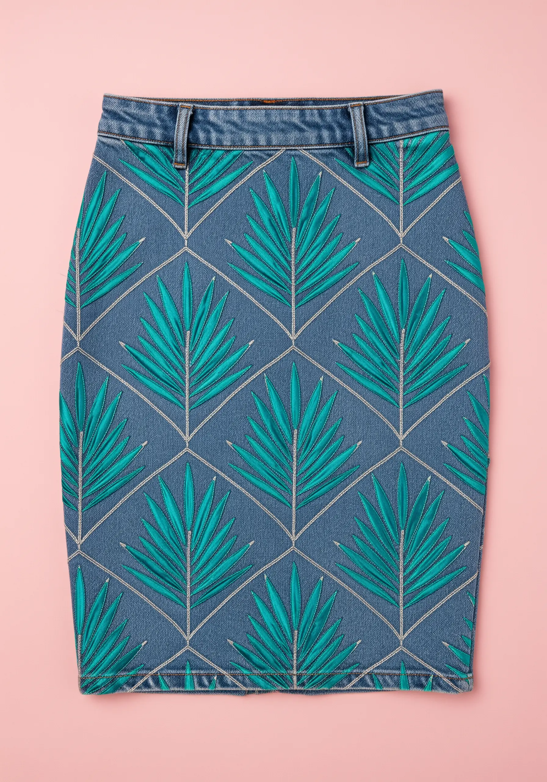 A geometric pattern of teal palm leaves stitched inside a grid on a denim skirt.