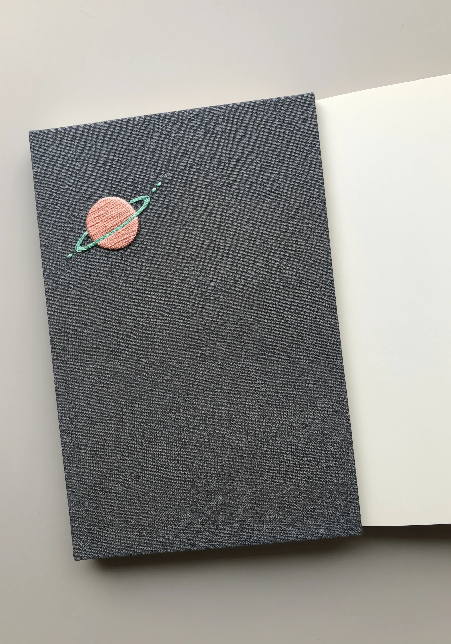 A small embroidered planet with rings on a dark grey notebook cover.
