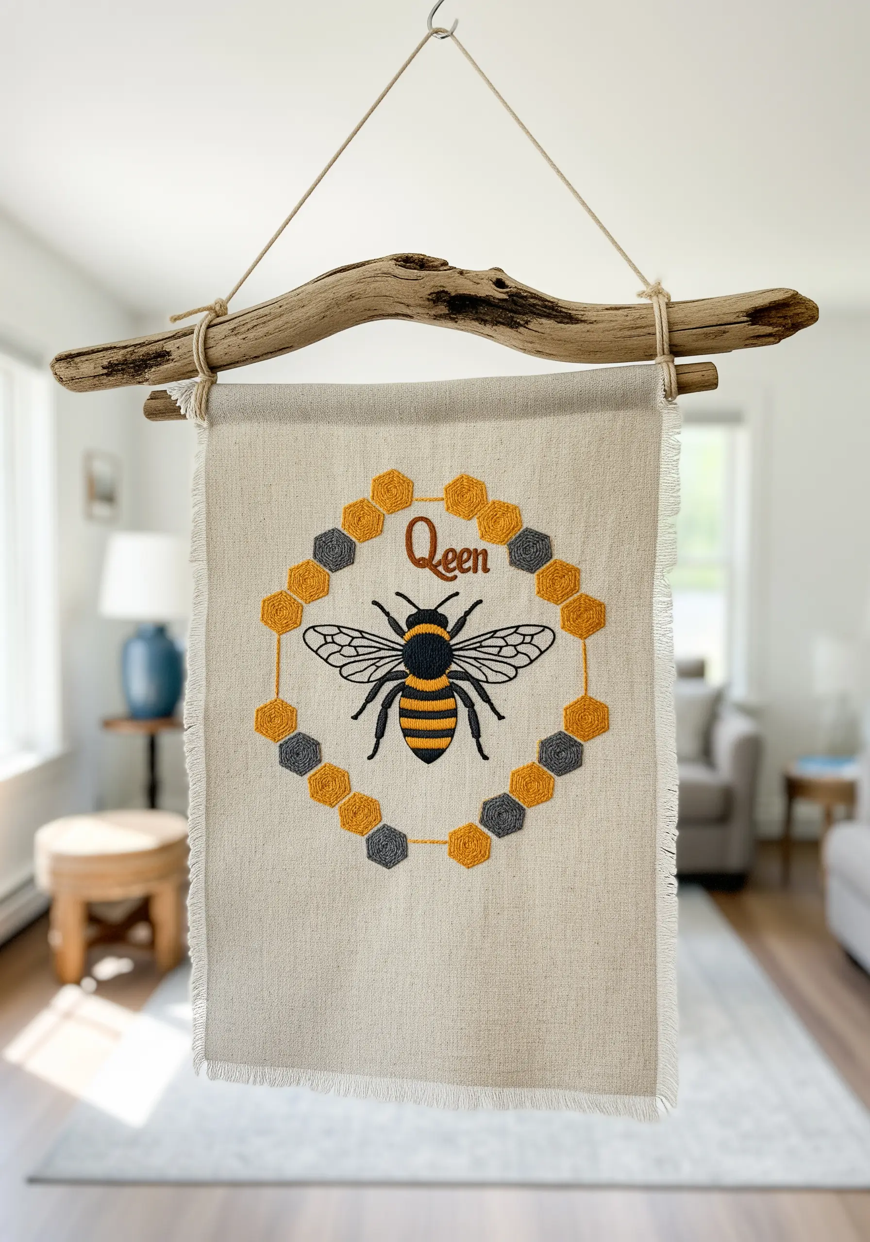 A bee embroidery on a linen banner, framed by a border of honeycomb shapes.