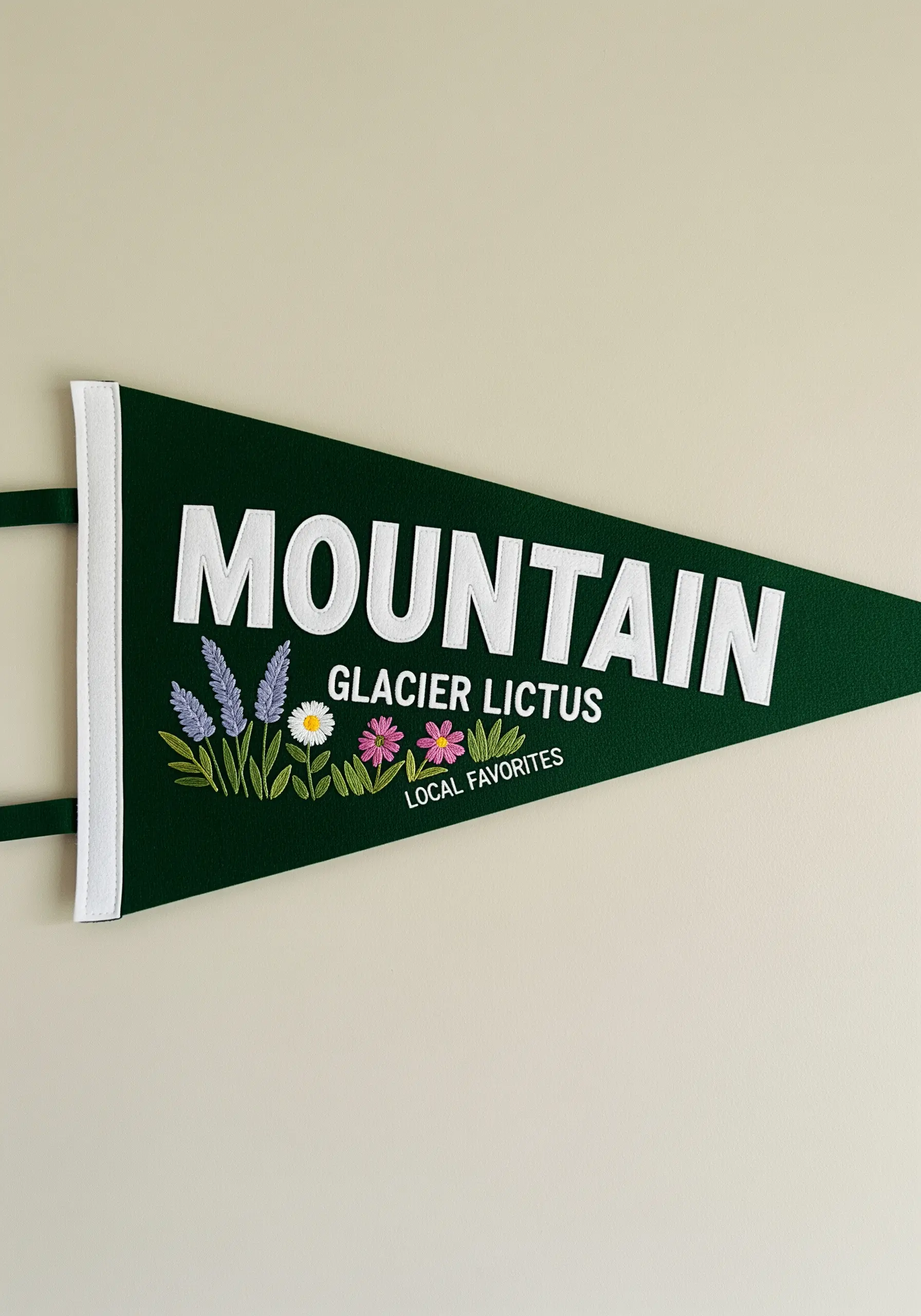 A green felt pennant flag with the word 'Mountain' and a small spray of embroidered wildflowers