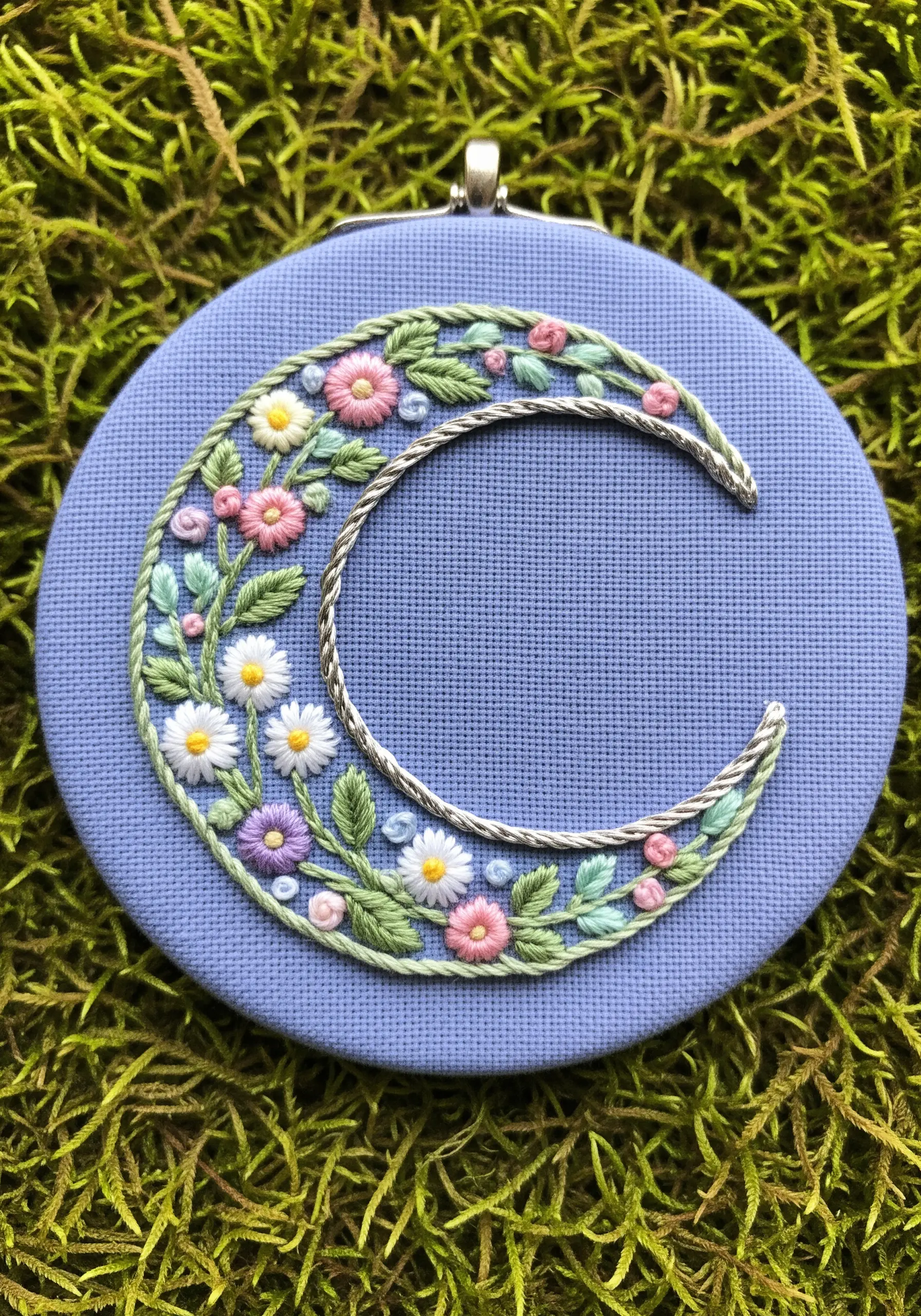 A crescent moon outlined in silver thread and filled with miniature embroidered flowers.