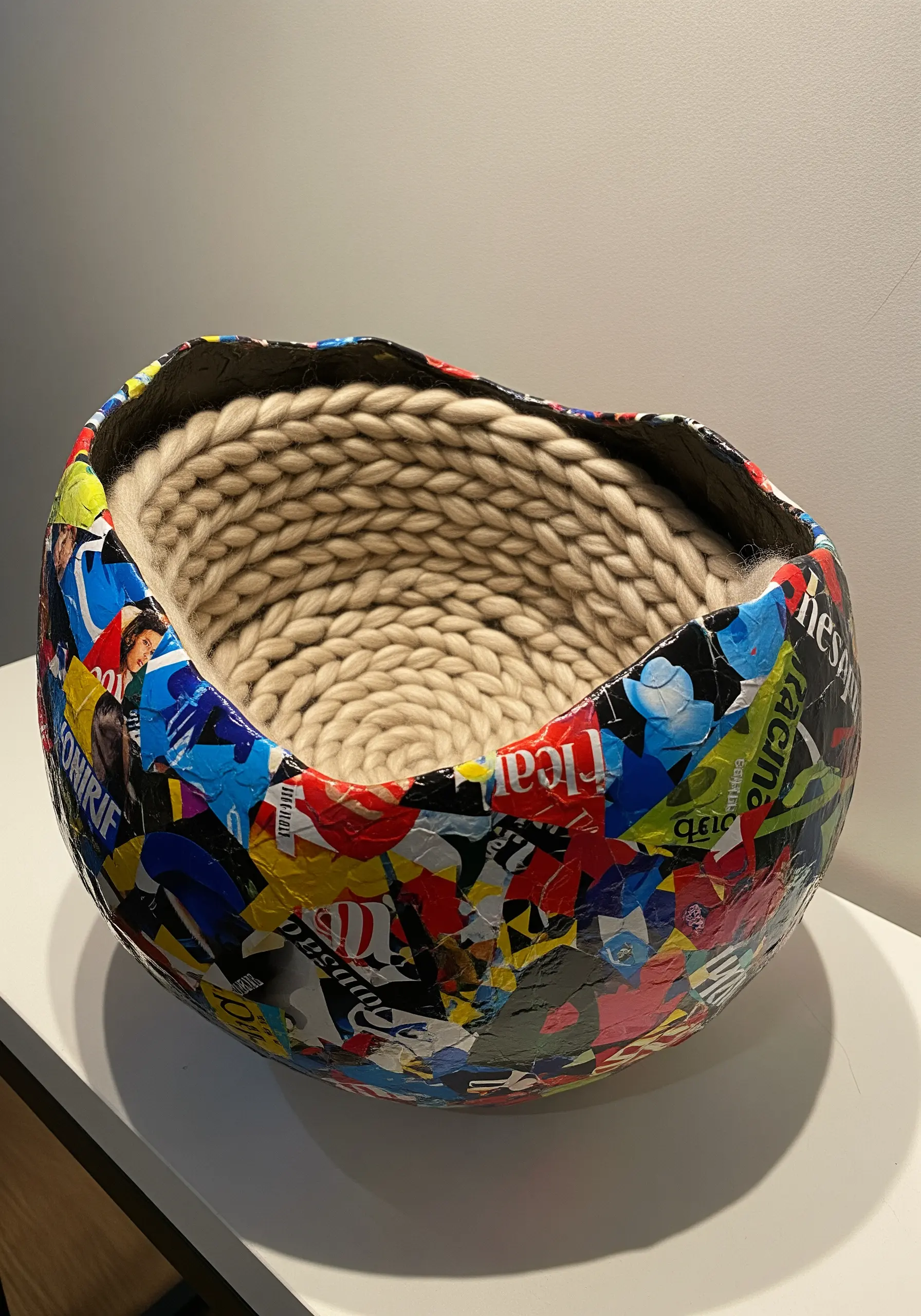 A bowl made of colorful magazine collage on the outside and soft, coiled rope on the inside.
