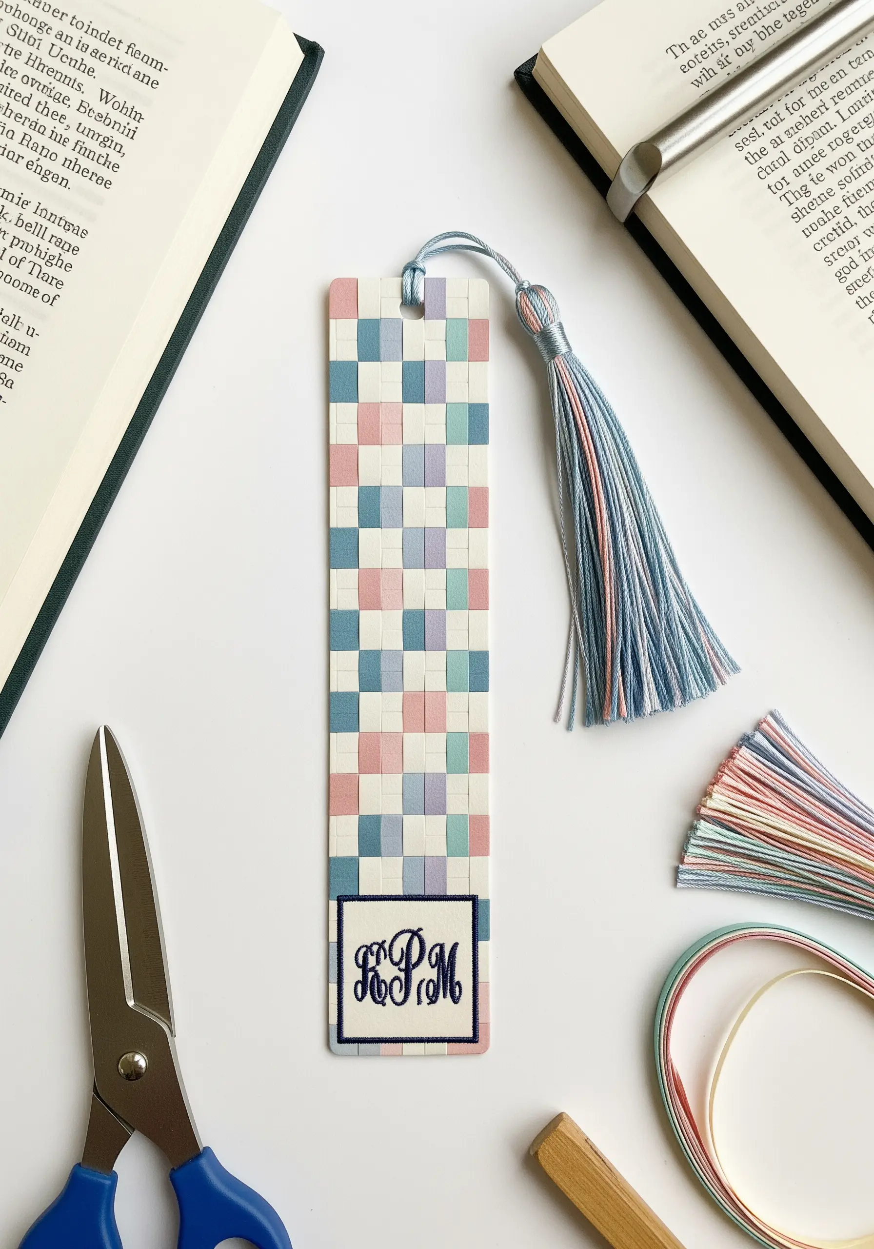 A bookmark made of woven paper strips in pastel colors with an embroidered monogram at the bottom.
