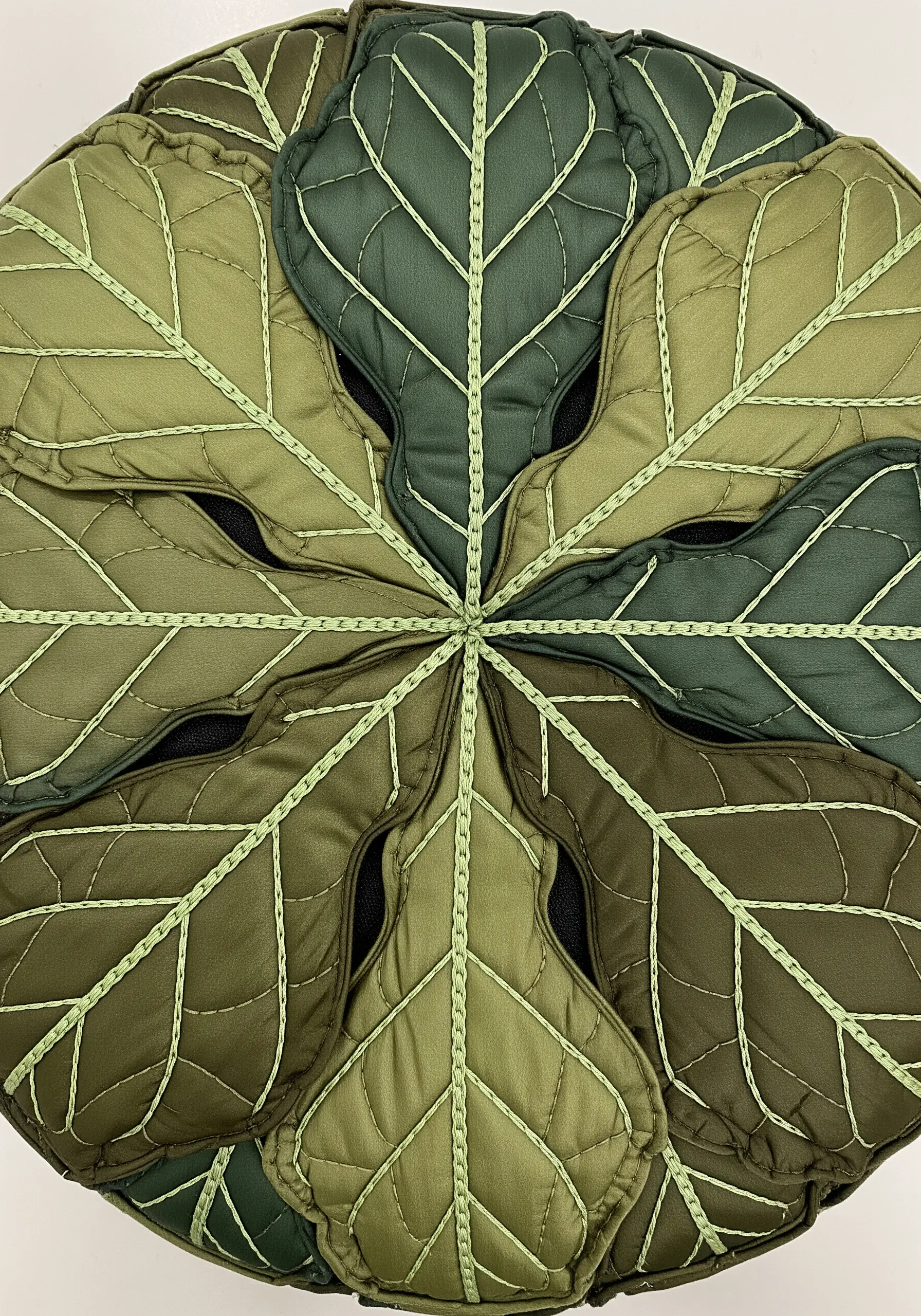 A quilted and stitched trivet made of puffy, segmented green leaf shapes.