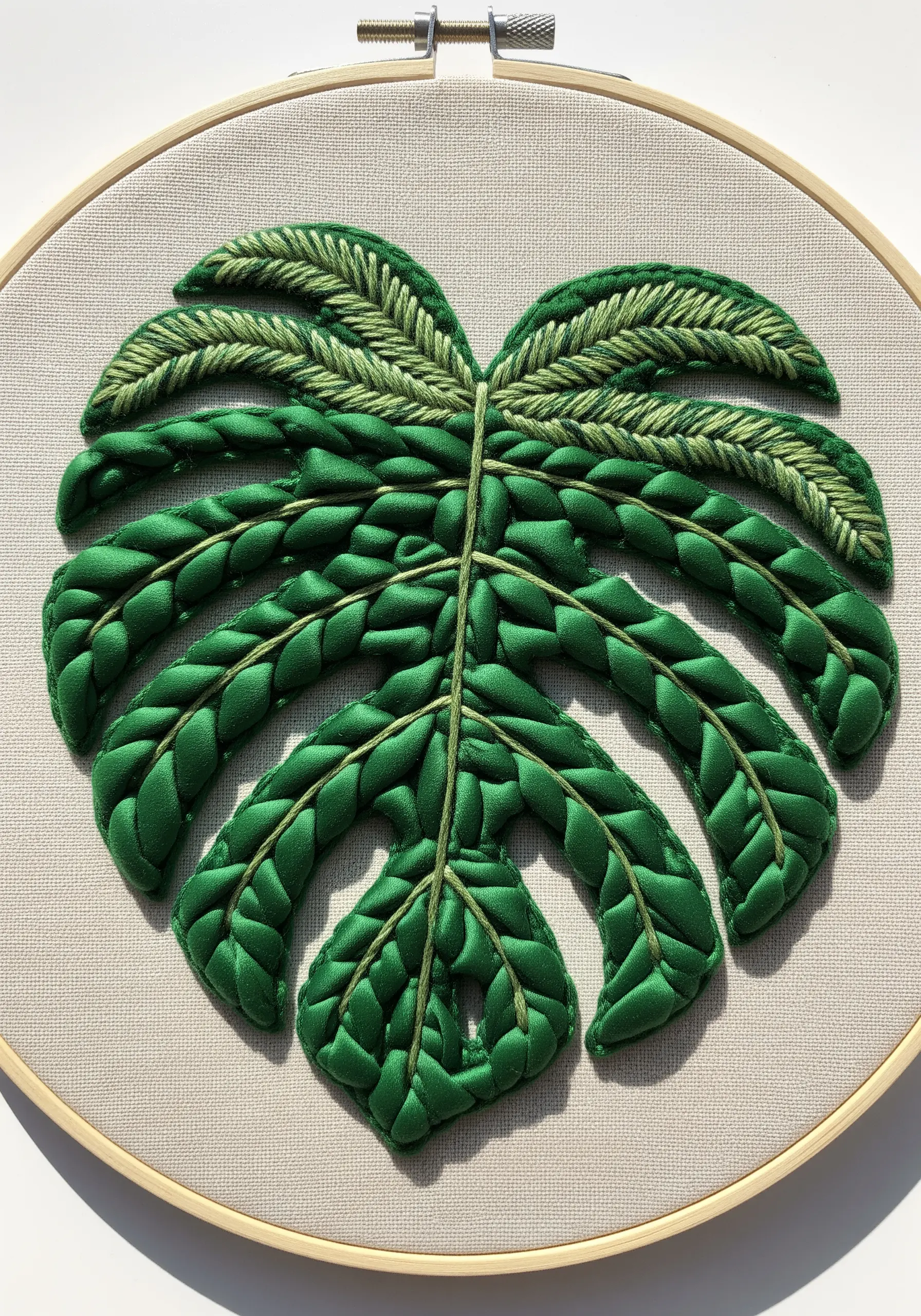 A monstera leaf embroidered with green satin ribbon and lighter green cotton thread.