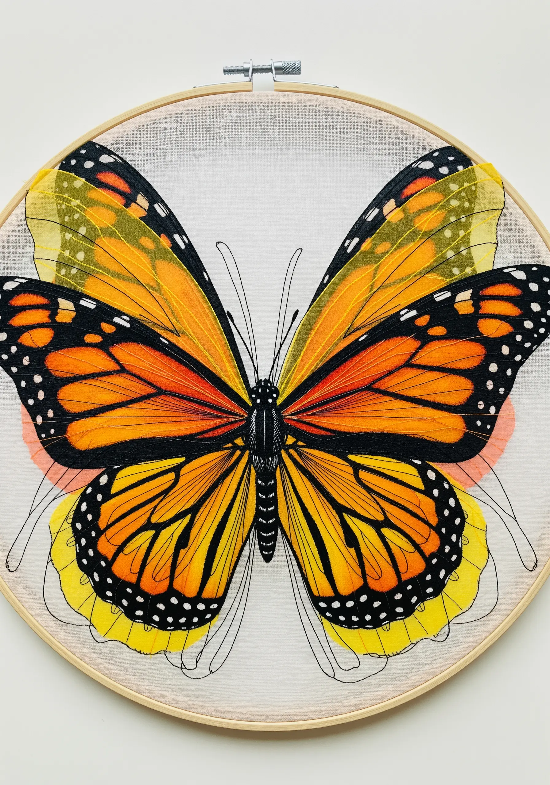 A monarch butterfly in a hoop, with sheer yellow and orange fabric wings outlined in black thread.