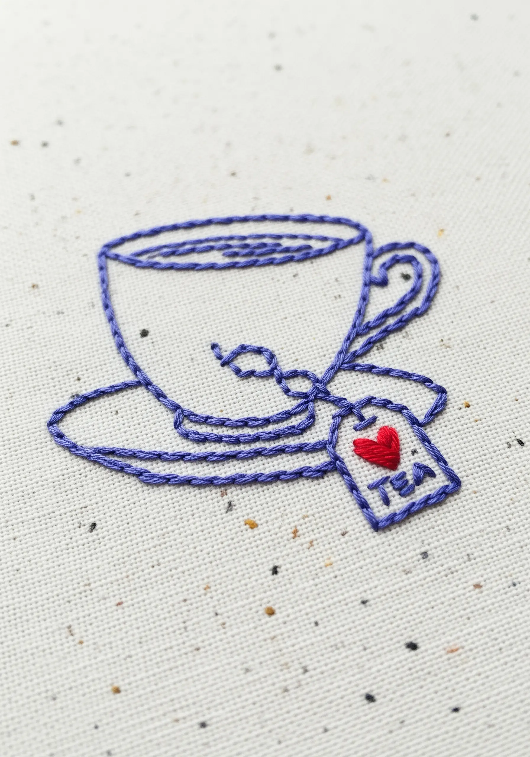 An outline of a teacup with a tea bag, stitched in purple thread.